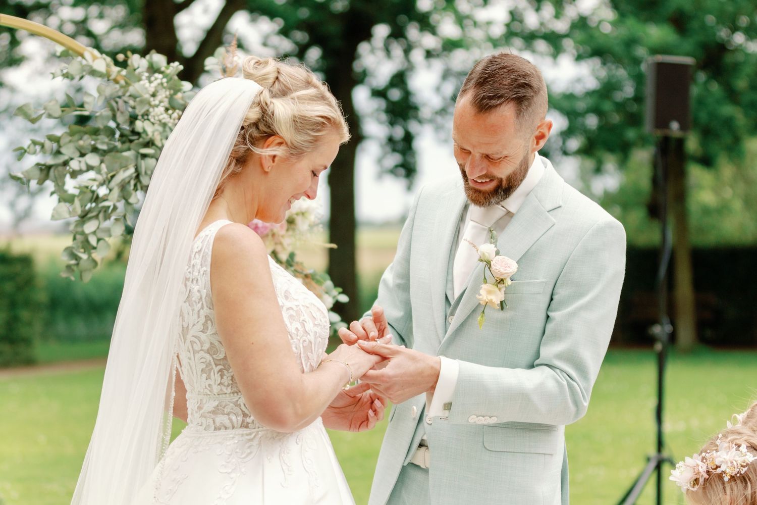 A romantic outdoor wedding ceremony features a couple exchanging rings under blooming trees in a garden setting.