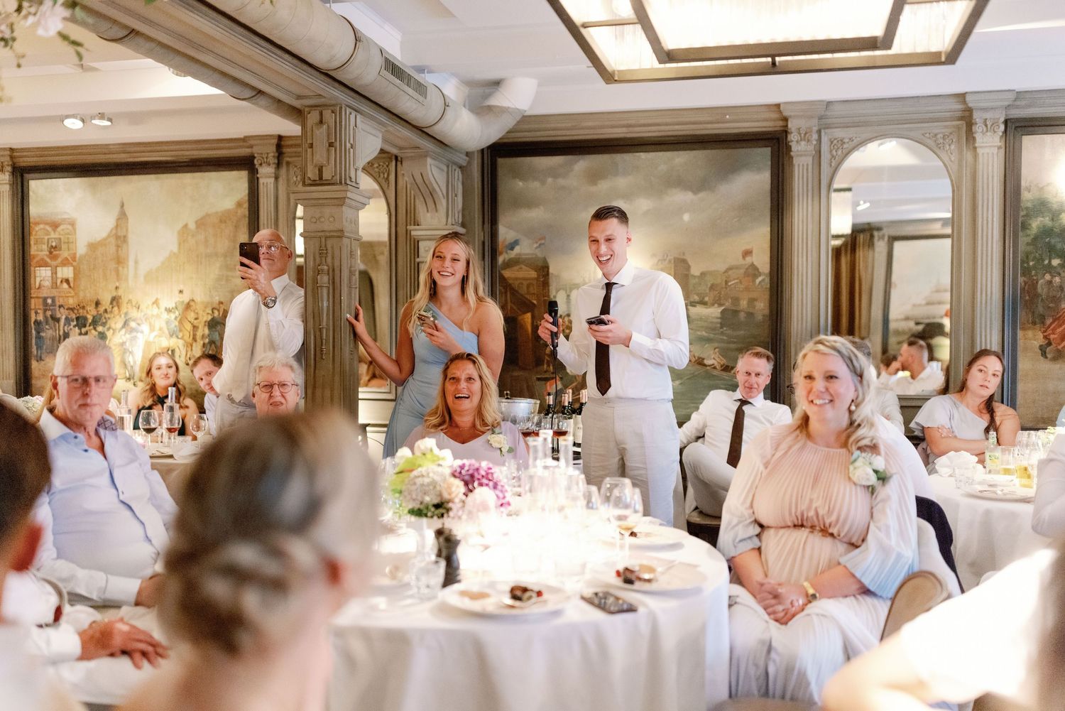 A panoramic sequence of wedding reception guests in white attire gathered around tables at an elegant indoor venue.