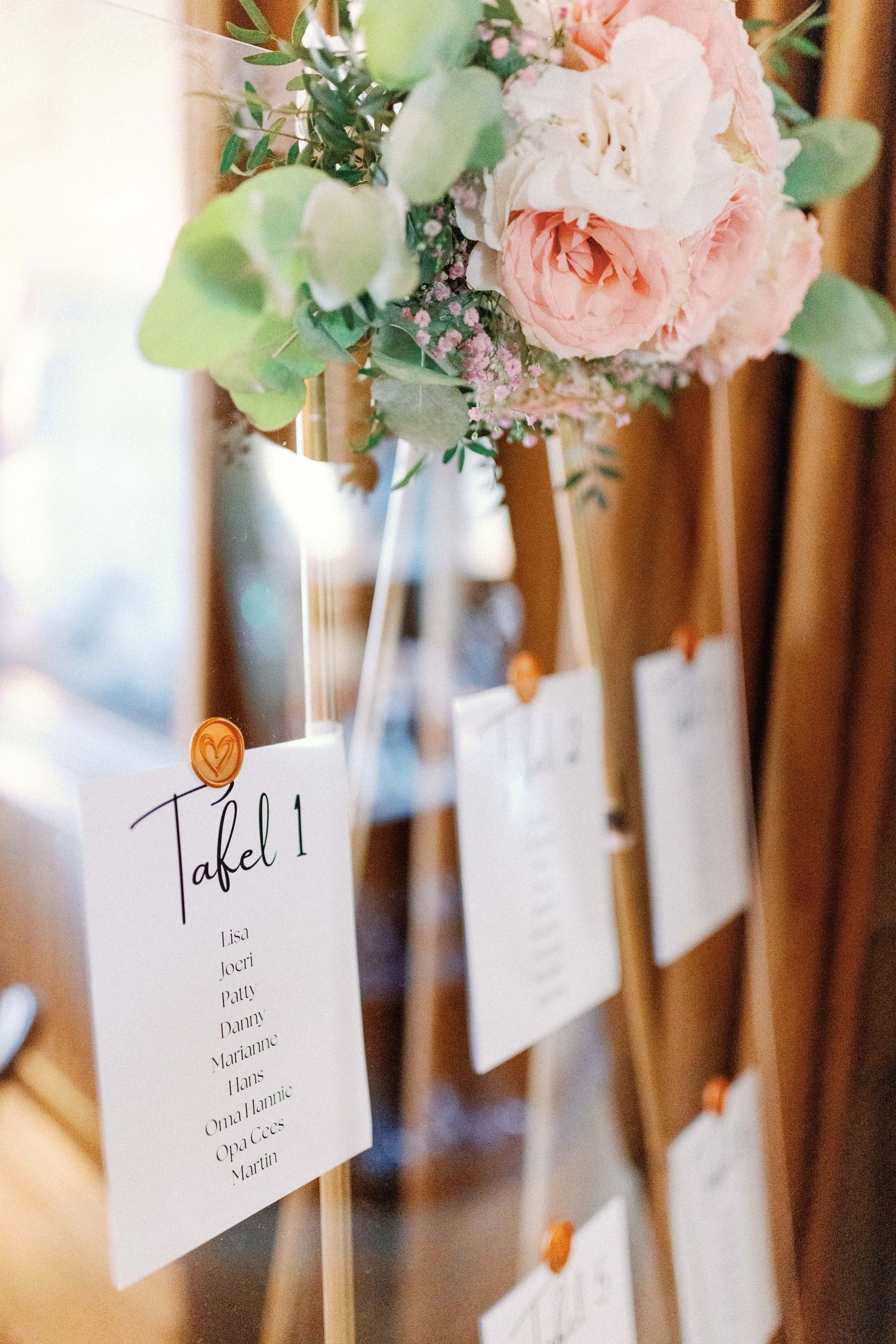 Wedding seating cards with delicate pink floral arrangements displayed on wooden posts create an elegant reception display.