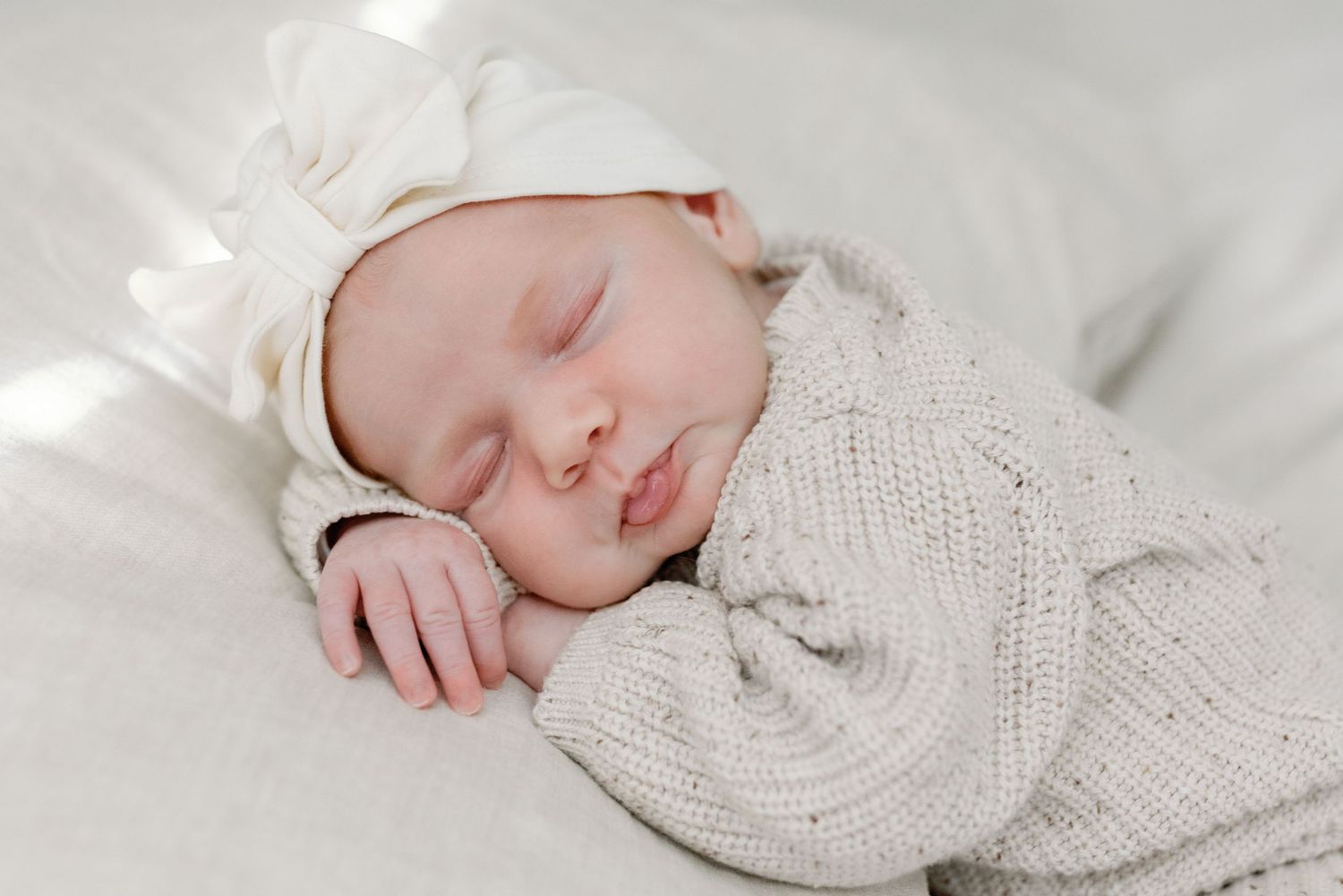 Sleeping newborn baby wrapped in soft white blankets lying on white bedding in peaceful slumber.