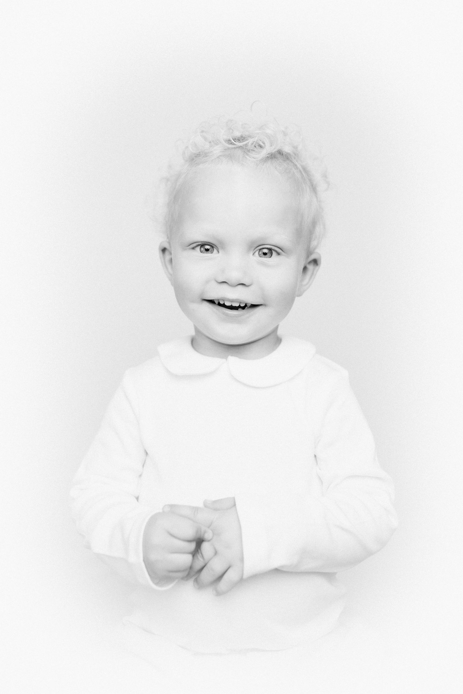 High key portrait of a baby in white against bright background.