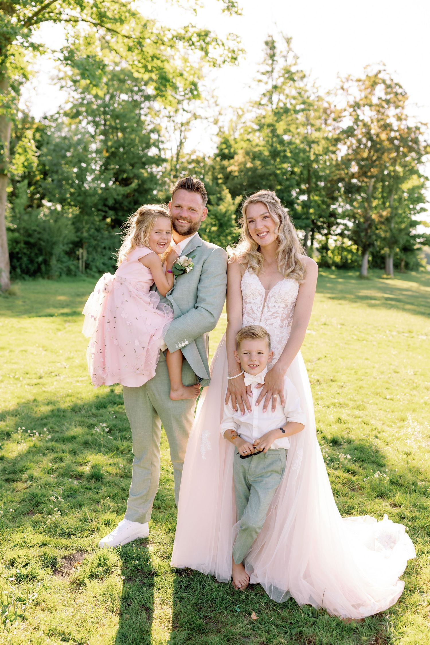 Family wearing light colored outfits shares joyful moments together in a sunny grassy field during golden hour.