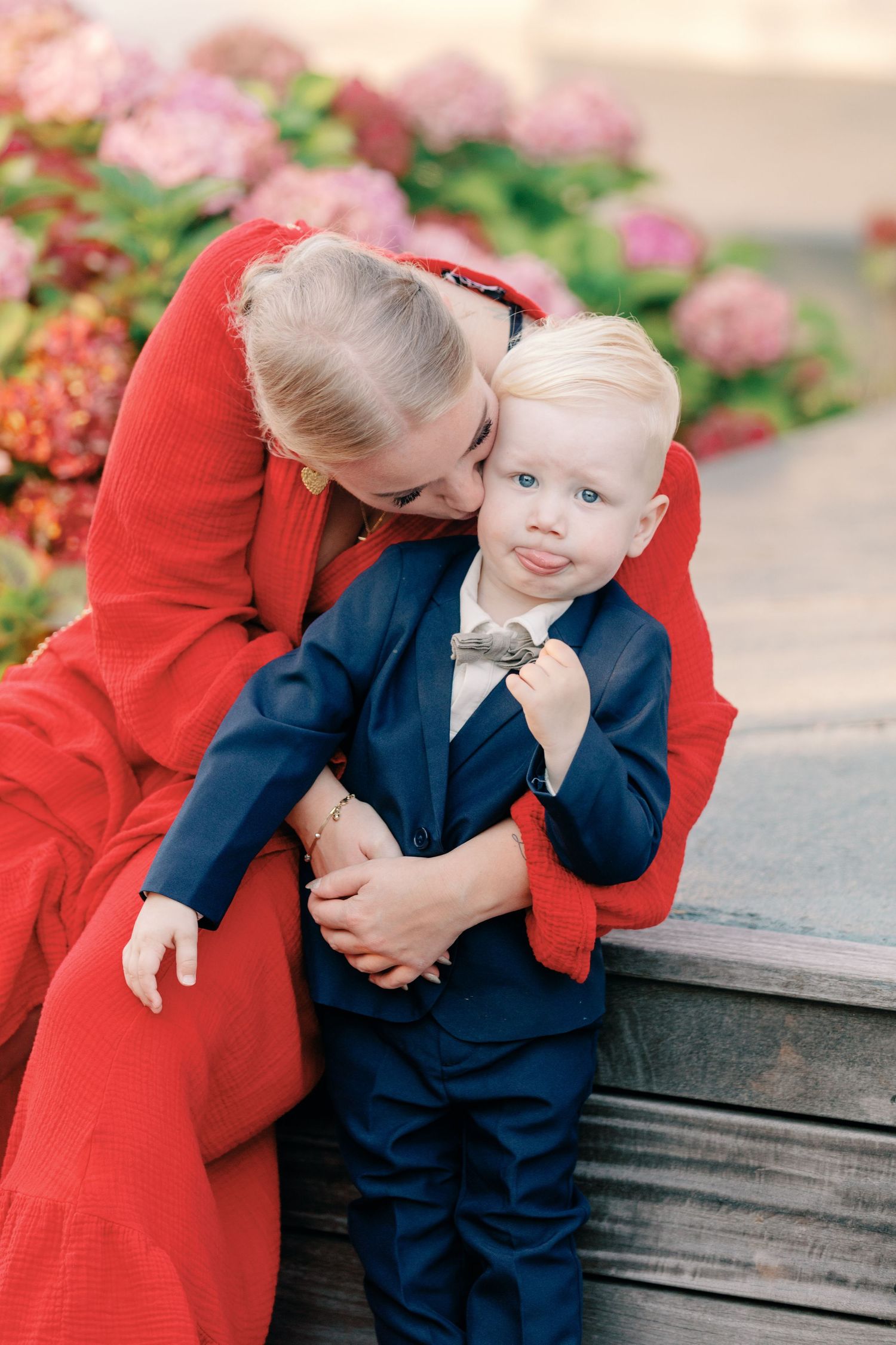 Young child in navy suit shares tender moment on wooden bench.