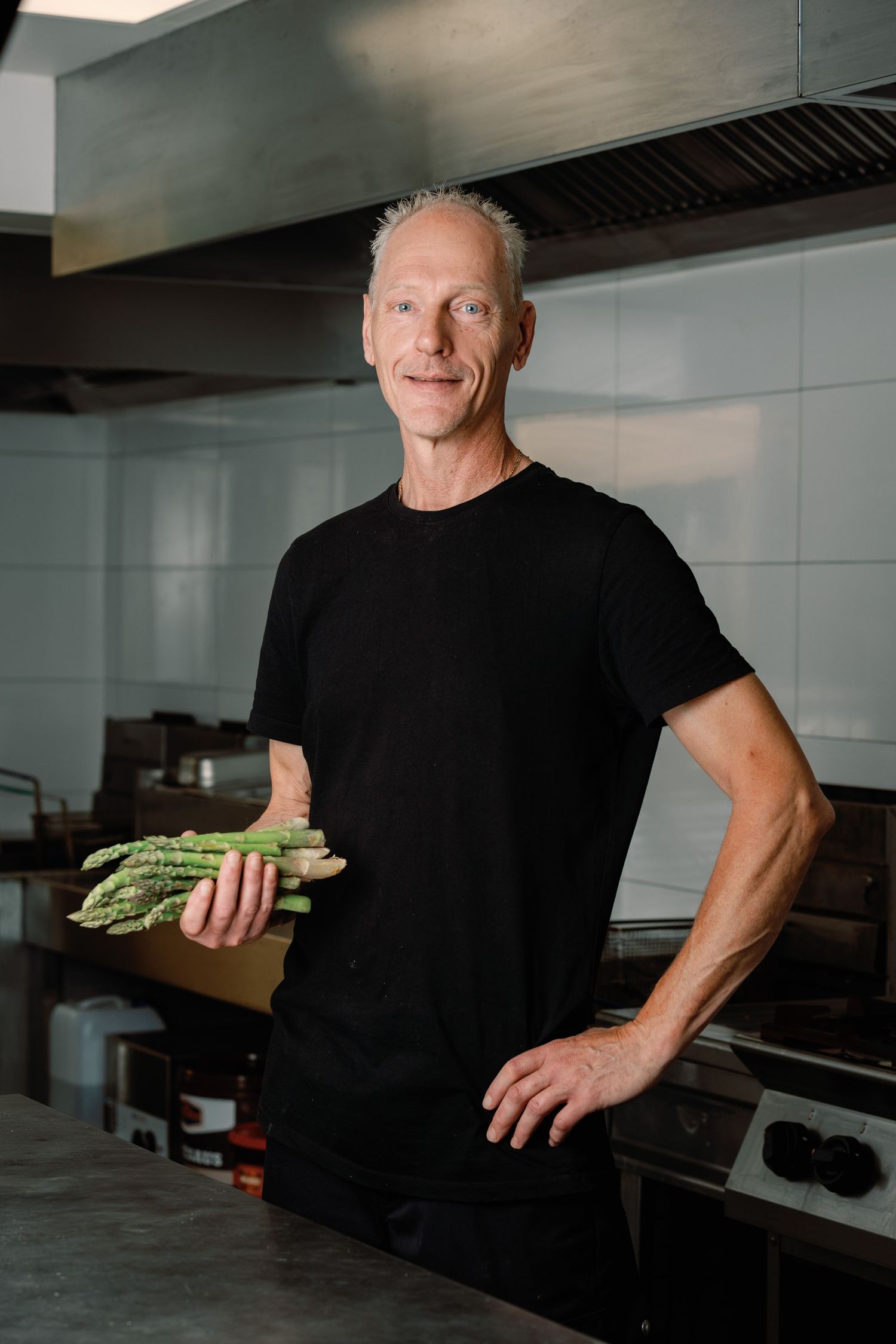 A sequence of five photos showing someone in black clothing holding fresh asparagus in a modern kitchen setting.