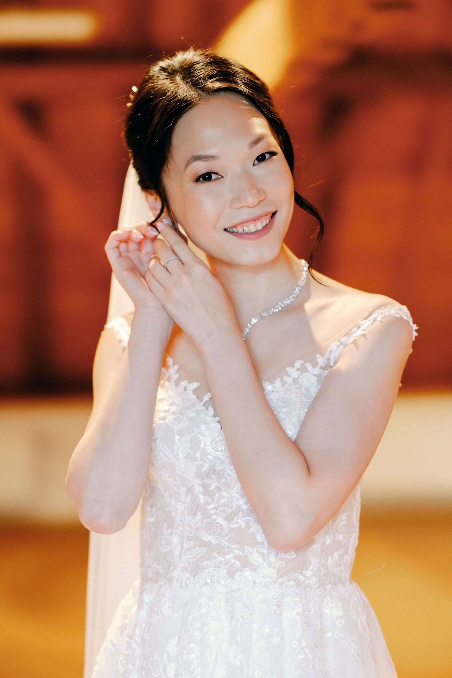 A person in a white lace dress poses joyfully against a warm-toned background.