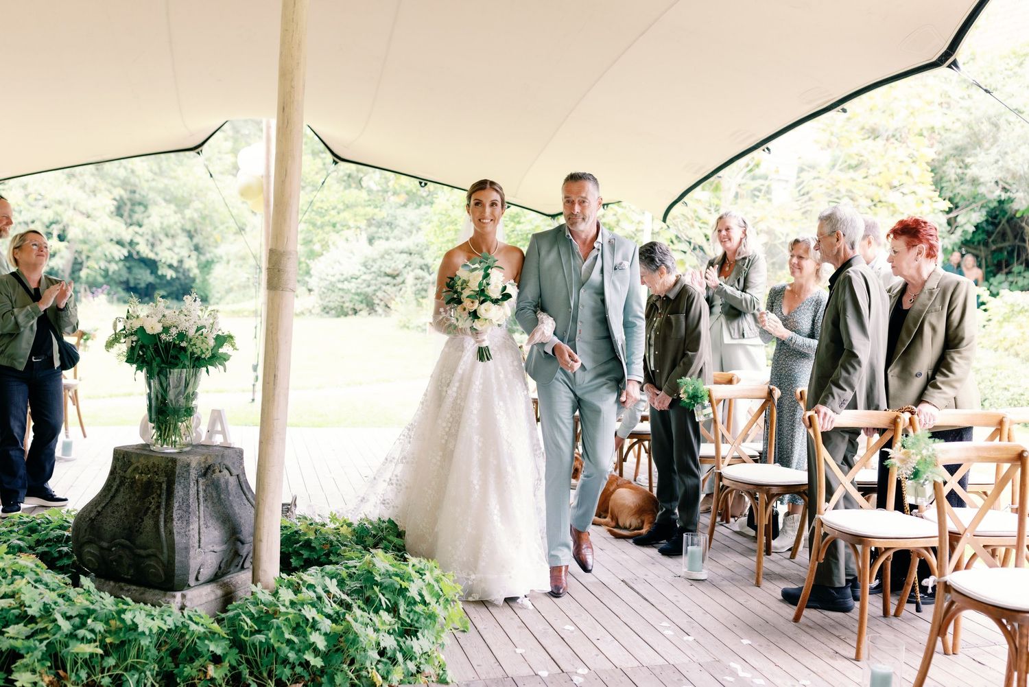 Wedding ceremony guests mingle and socialize under an elegant white tent during an outdoor reception celebration.