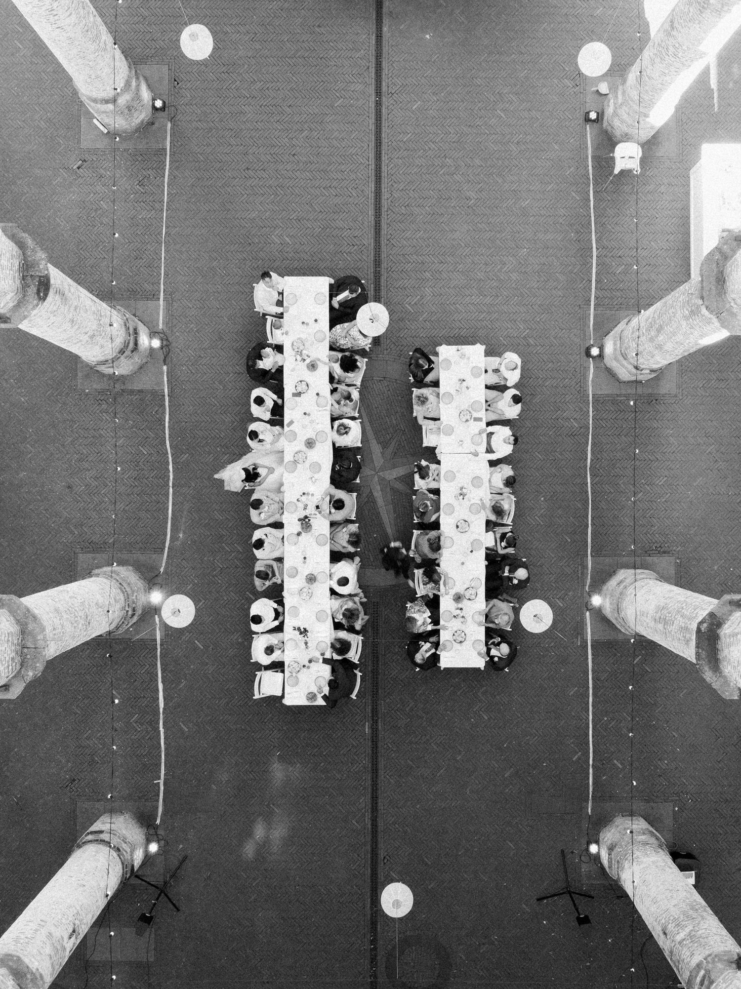 Overhead black and white view of two long dining tables with people seated during a formal gathering.