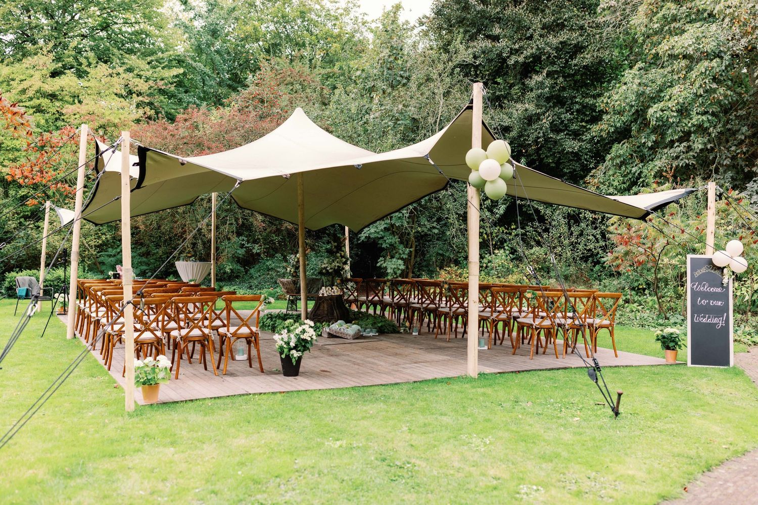 Outdoor wedding venue with white tent canopy, wooden chairs, and lush green garden setting for a romantic ceremony.