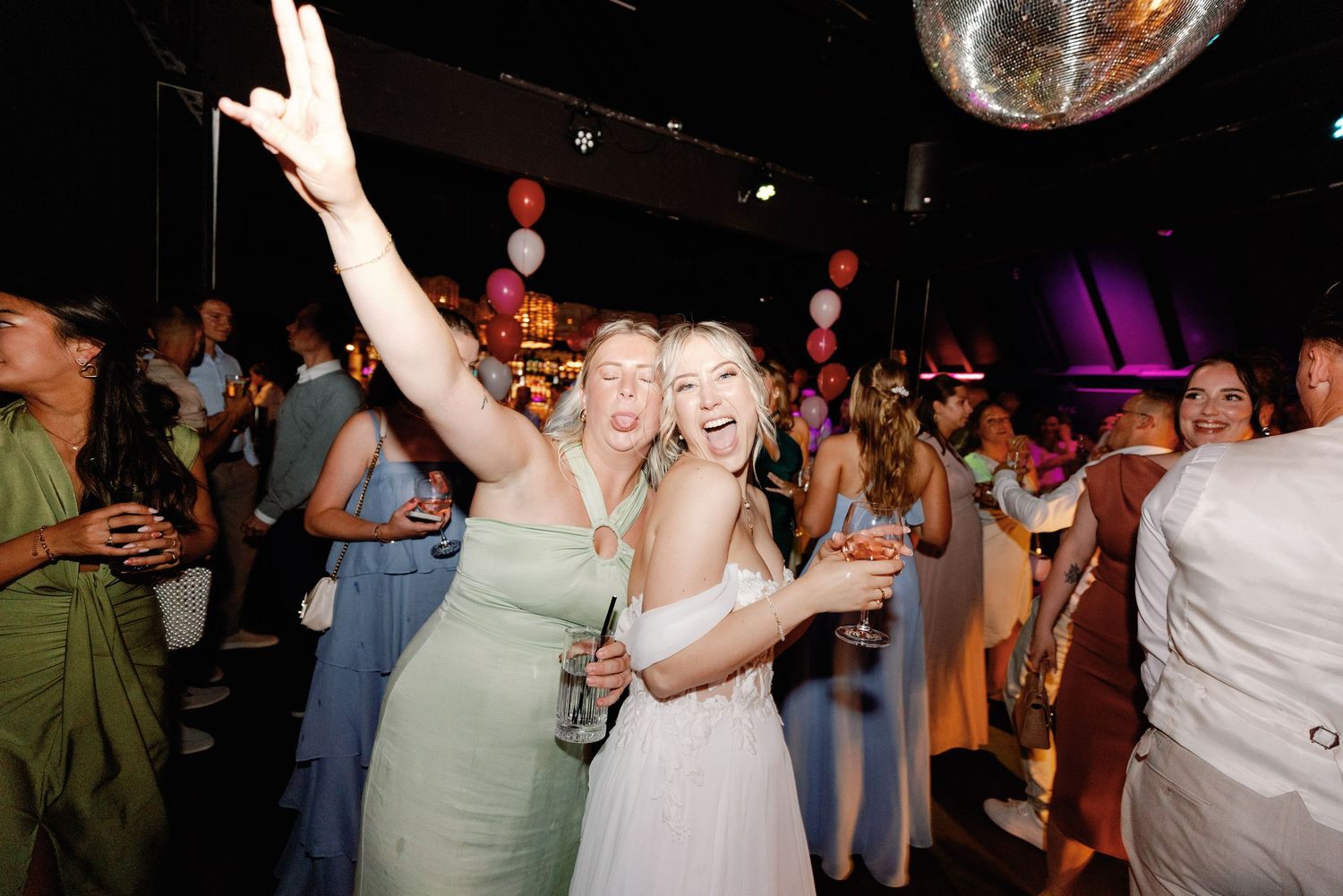 People dancing and celebrating at a lively wedding reception with disco ball and party lights illuminating the dance floor.
