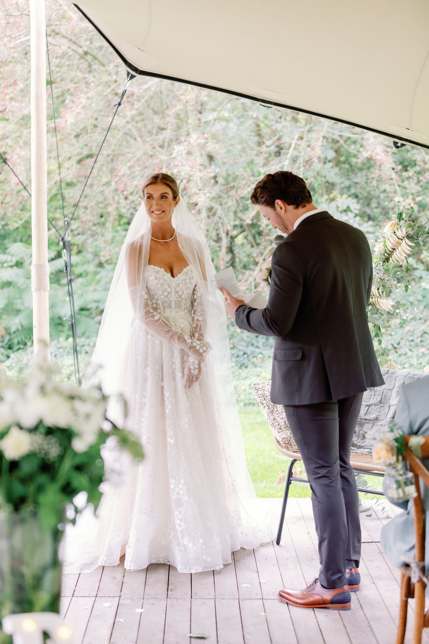 A couple shares an intimate moment during their wedding ceremony on a rustic wooden deck surrounded by greenery.