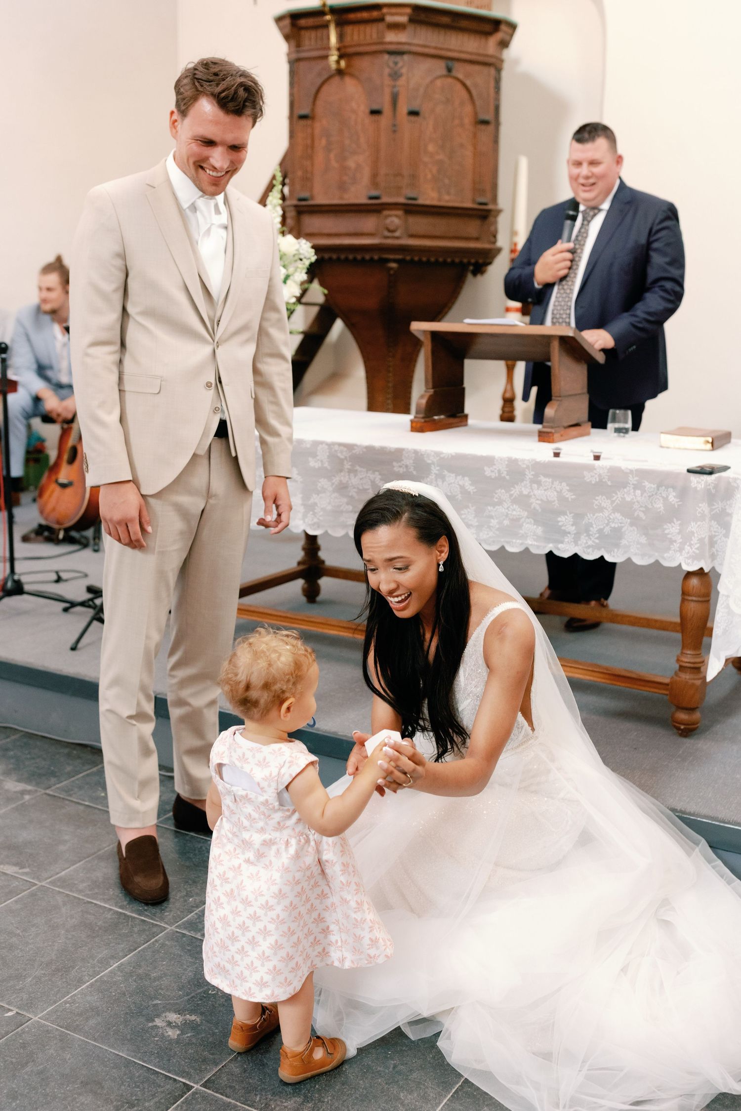 A touching moment during a wedding ceremony as a bride in white dress interacts with a small child in a church setting.