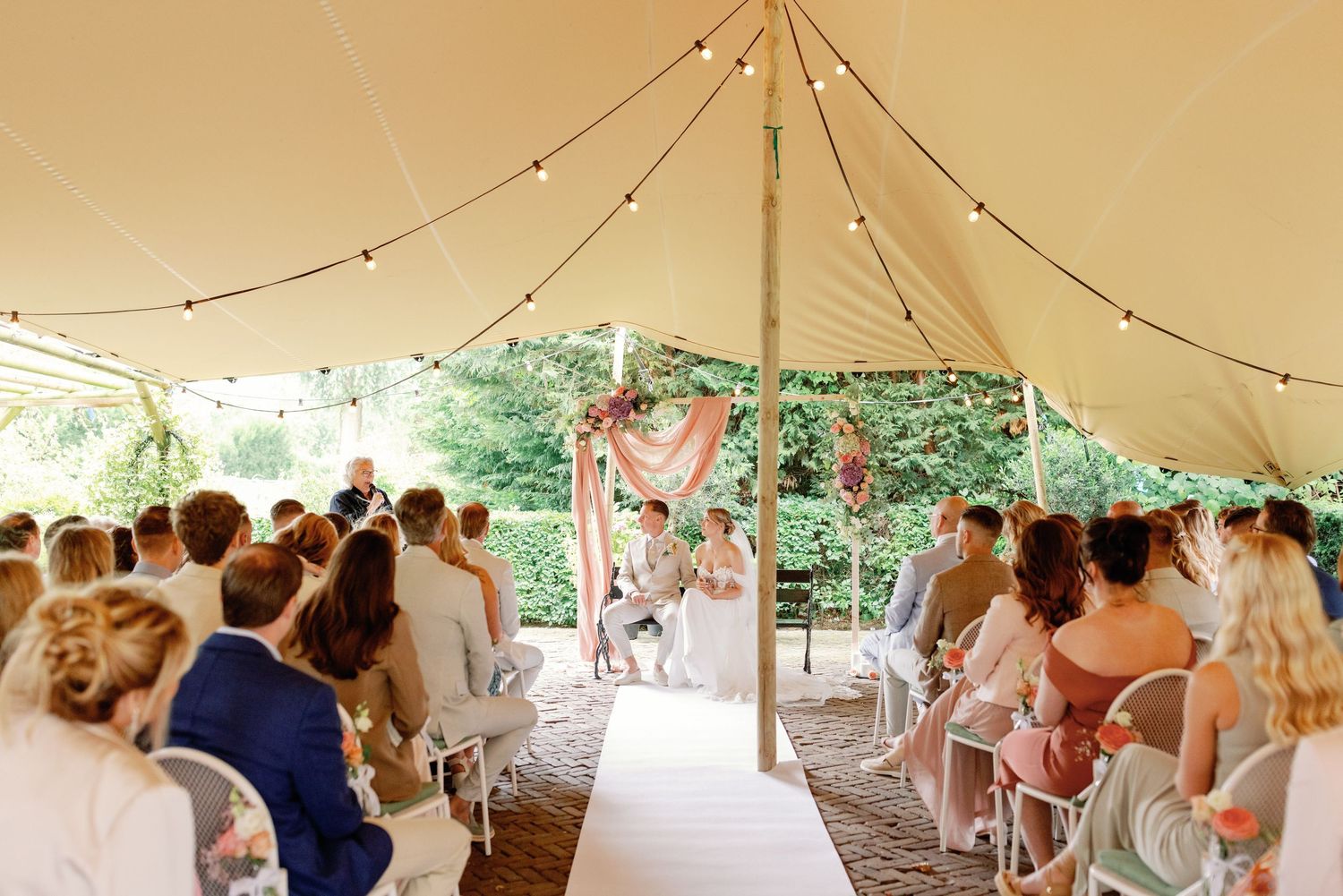 Wedding guests gather under an elegant white tent canopy during an outdoor celebration.