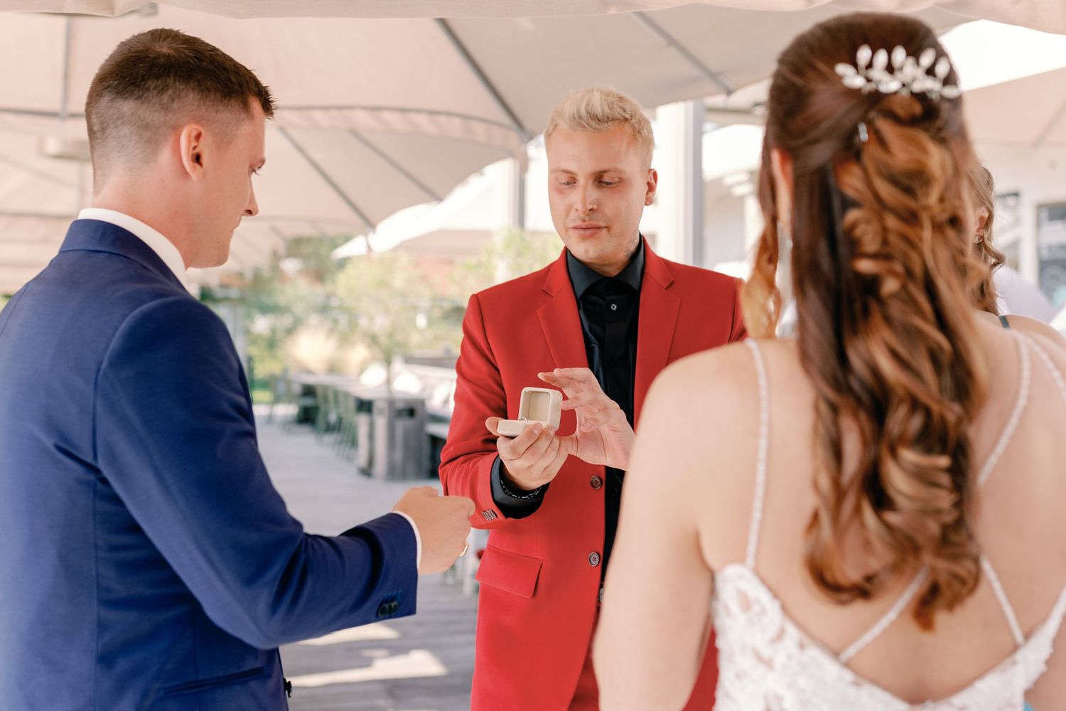 A wedding ceremony moment under a white canopy with an officiant in a red jacket.