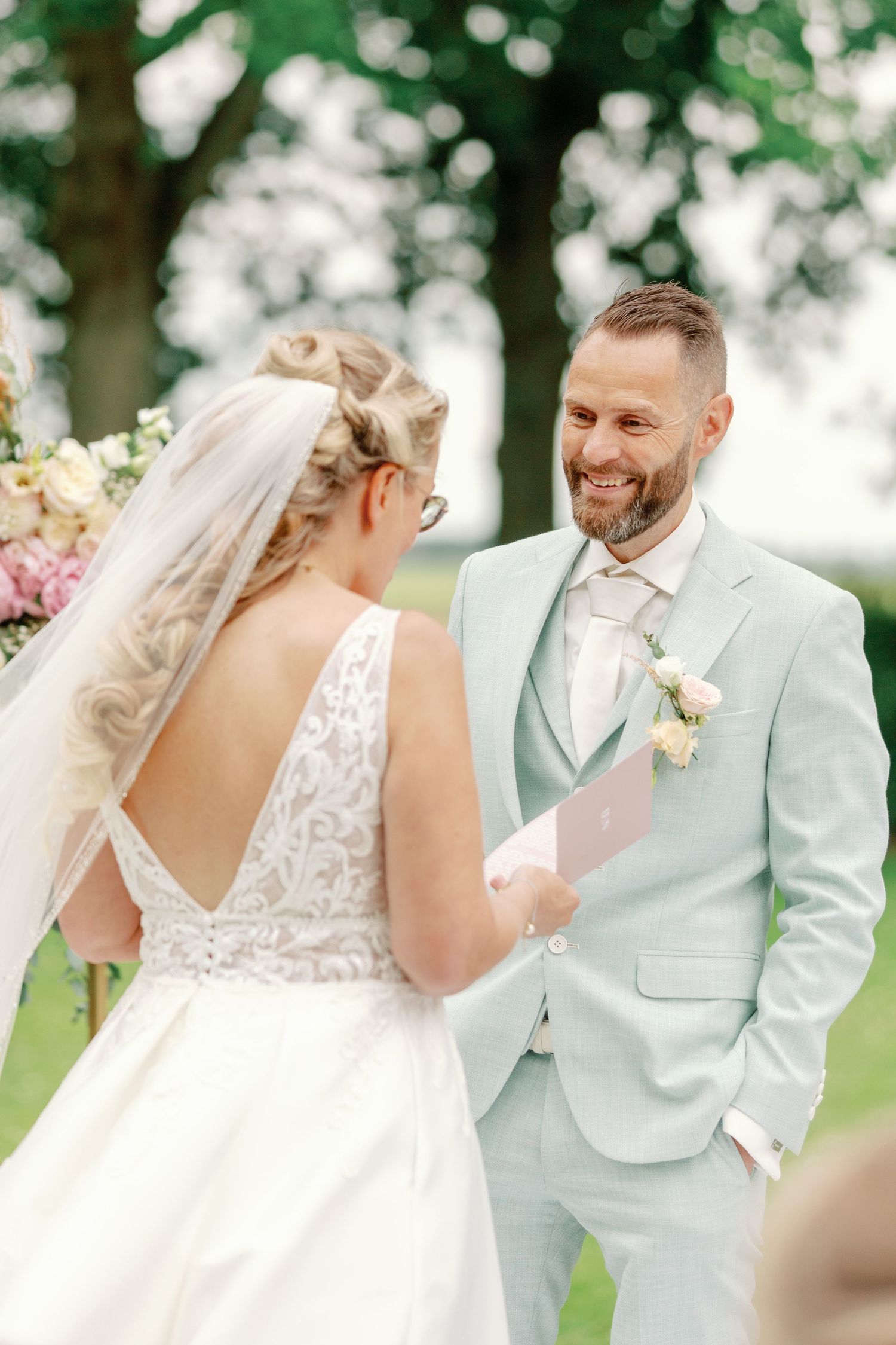A joyful wedding couple shares candid moments outdoors, with the bride in white lace and groom in mint green suit.