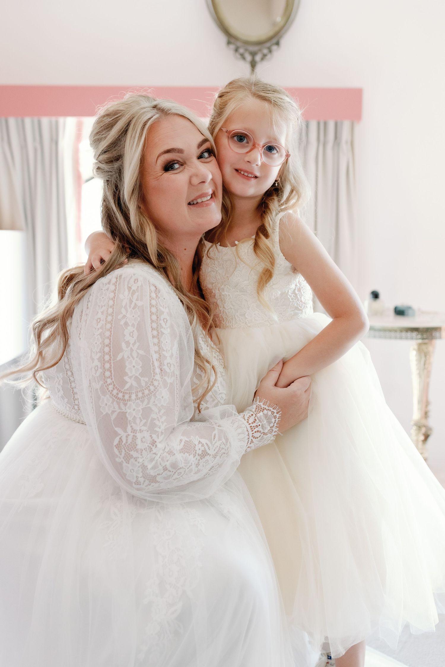 Two people in white lace dresses share joyful moments together in a bright, airy room.