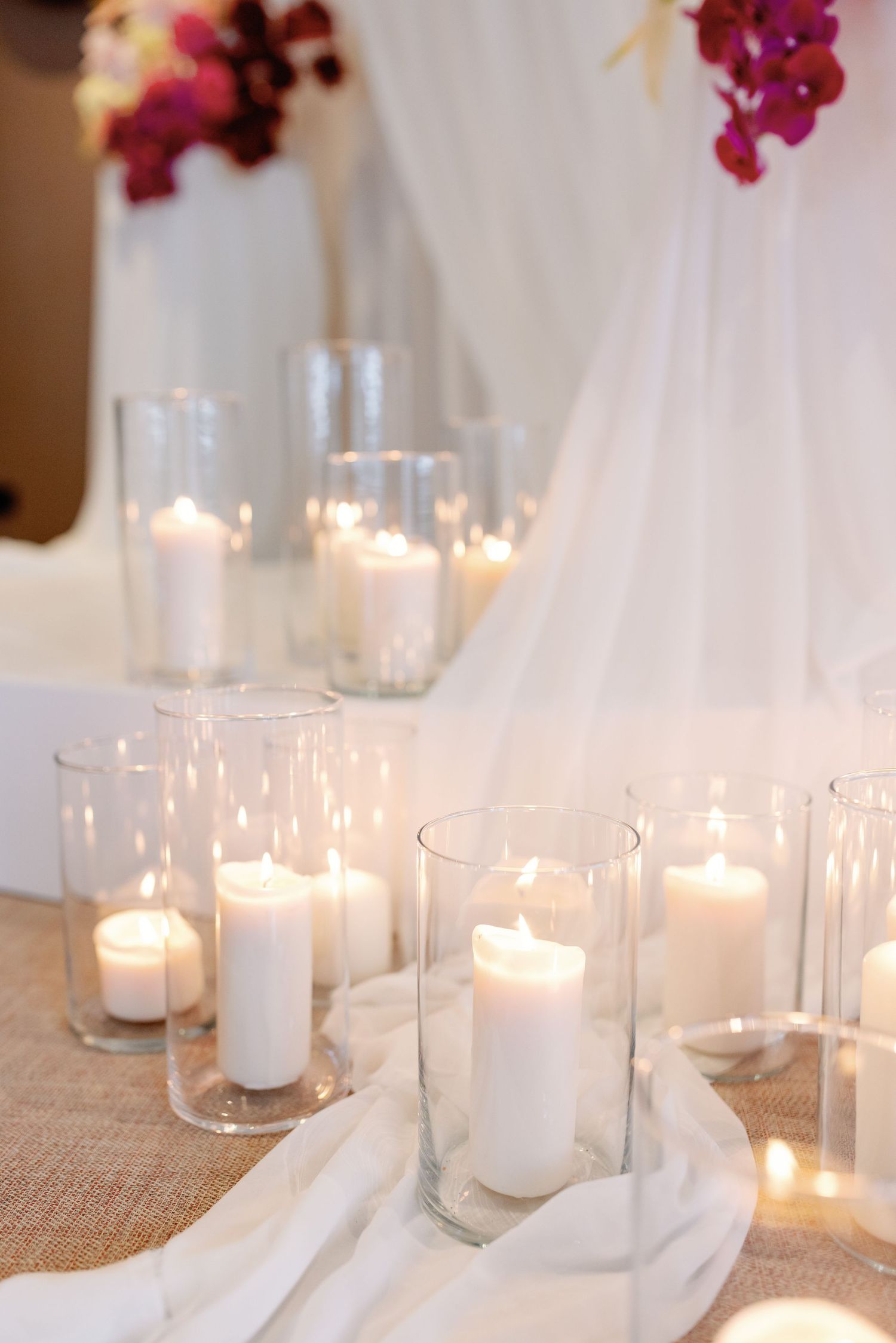 White pillar candles glowing in glass holders on a textured burlap runner for an elegant table setting.