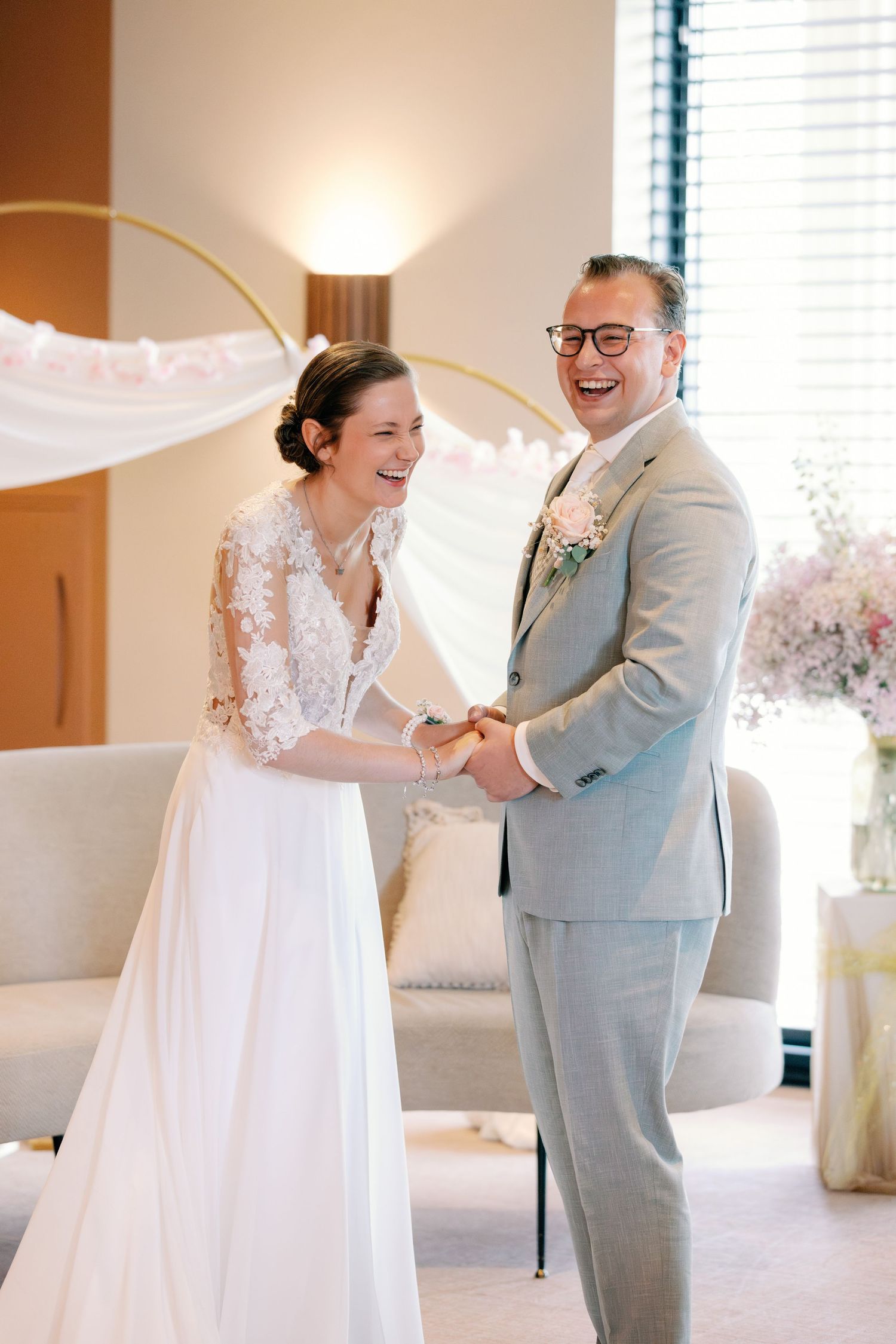 Happy bride and groom holding hands and laughing during their wedding ceremony in an elegant indoor venue.