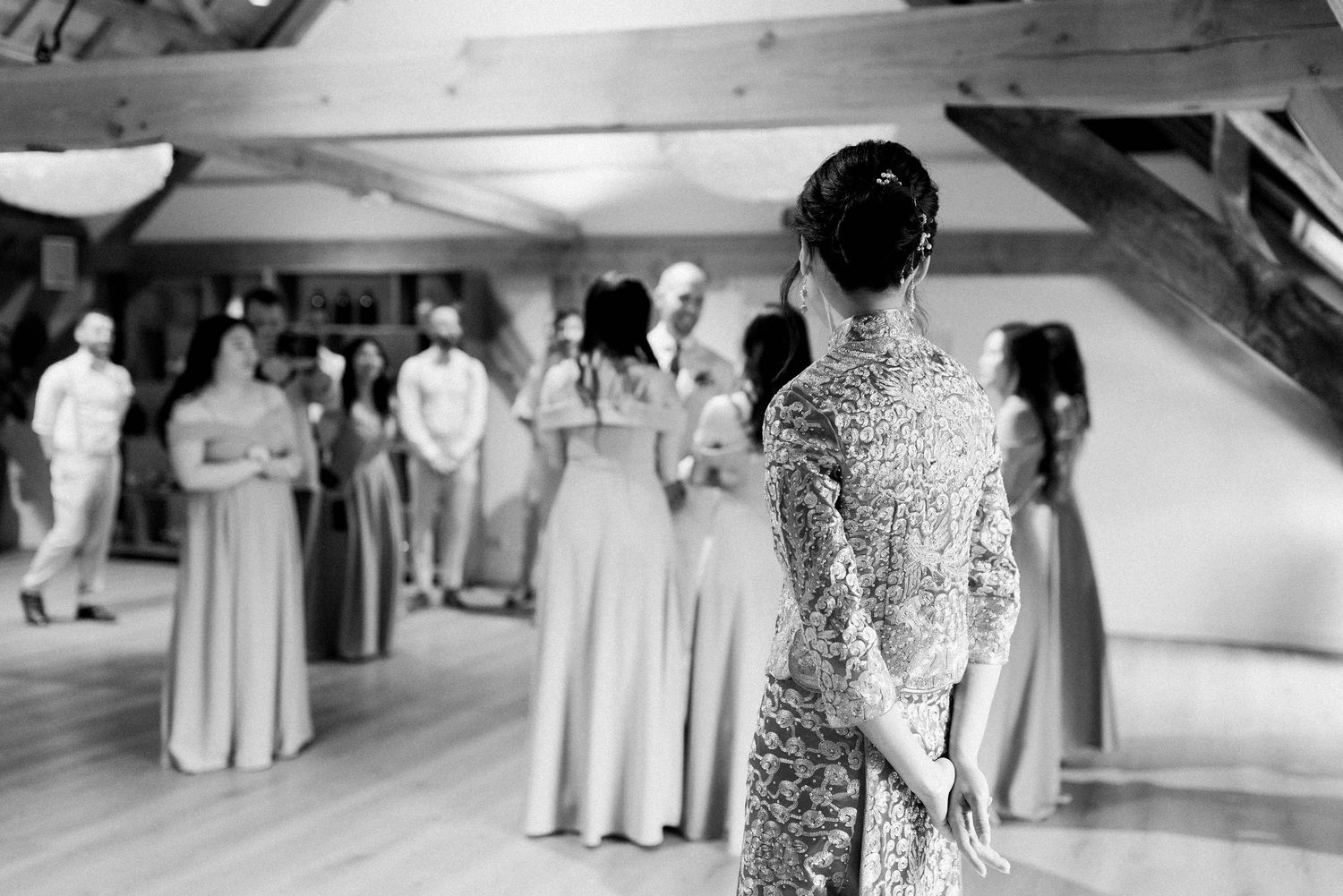 Wedding guests dance together on a wooden dance floor at an indoor reception venue.