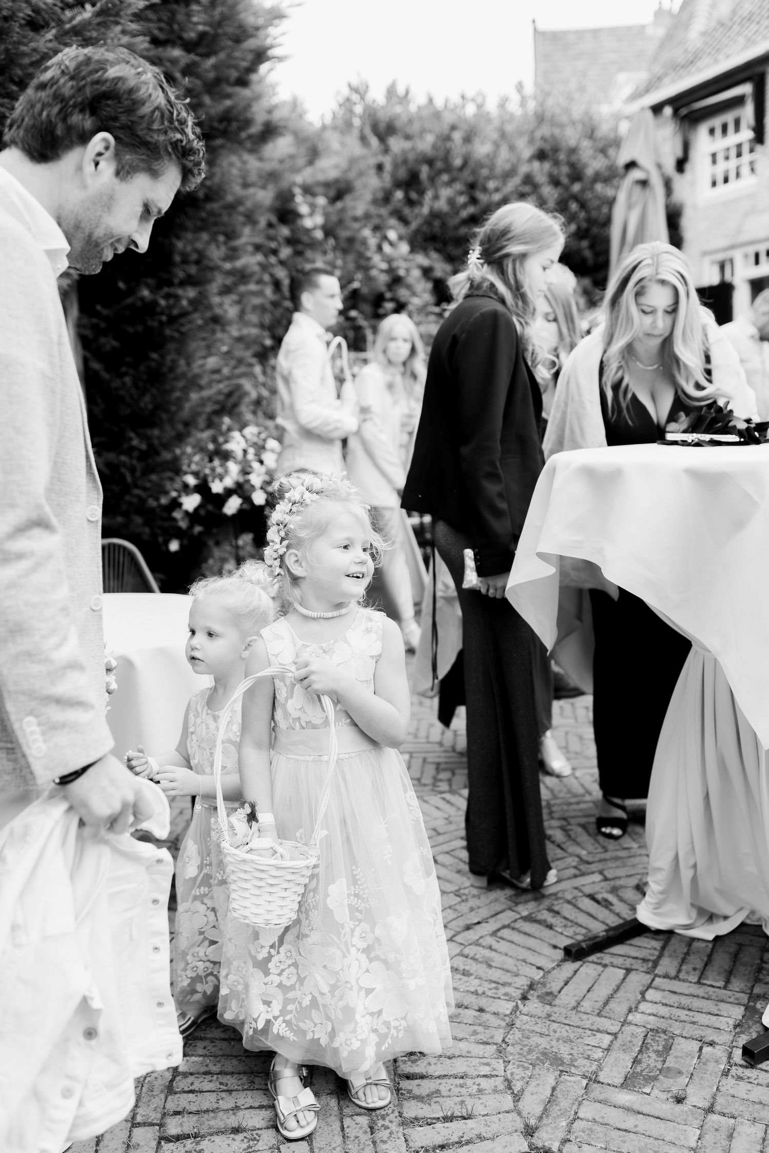 A group of children in formal white attire gather on a brick patio during what appears to be a wedding celebration.