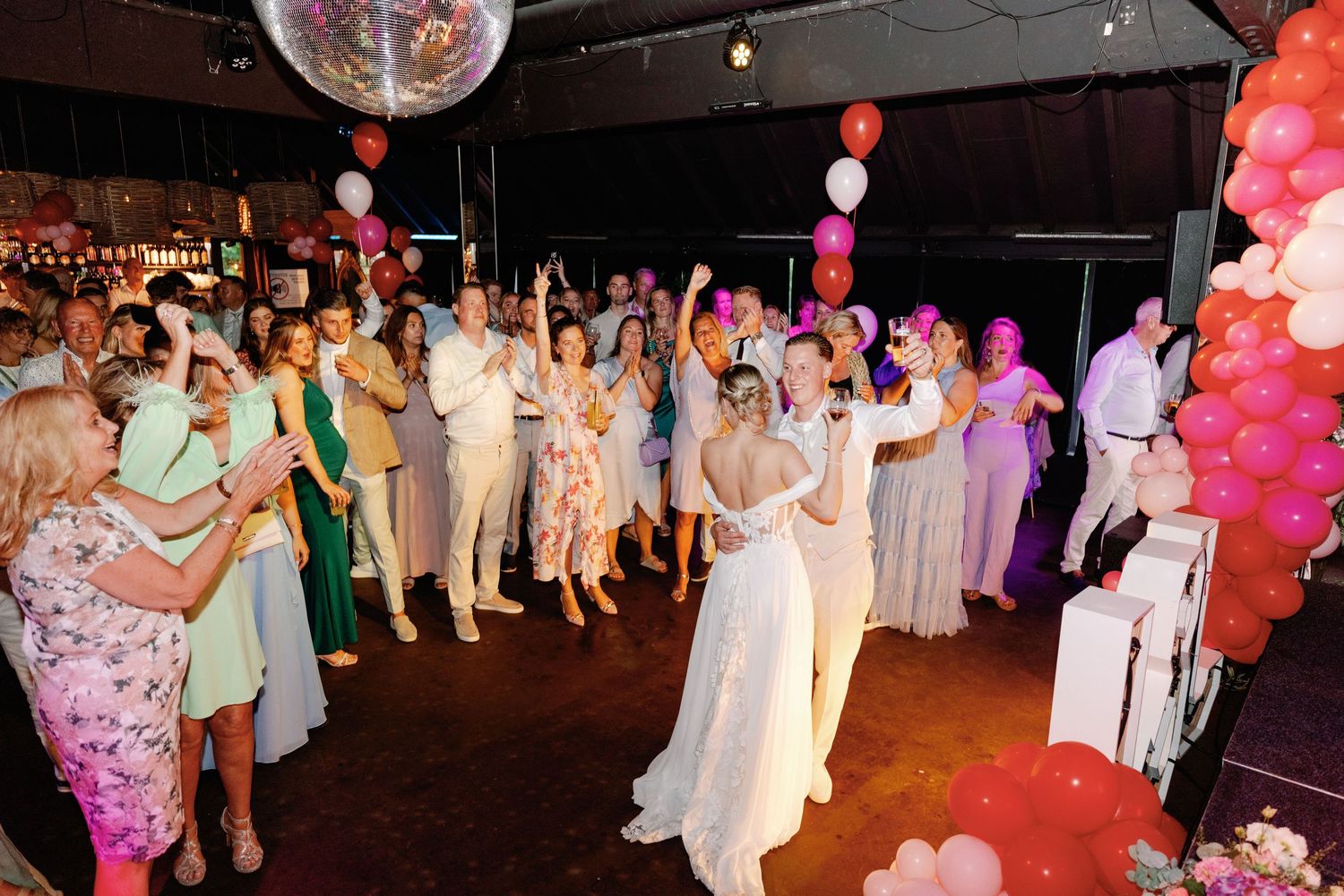 Wedding reception guests dance under a disco ball and colorful balloon decorations at an evening celebration.