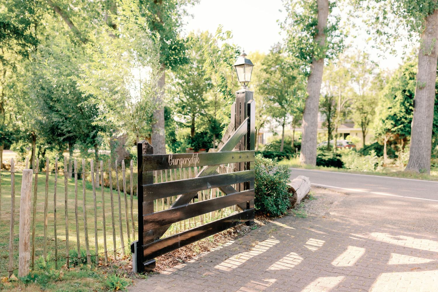 Wooden gate entrance to a tree-lined path in a park with dappled sunlight and fallen autumn leaves.