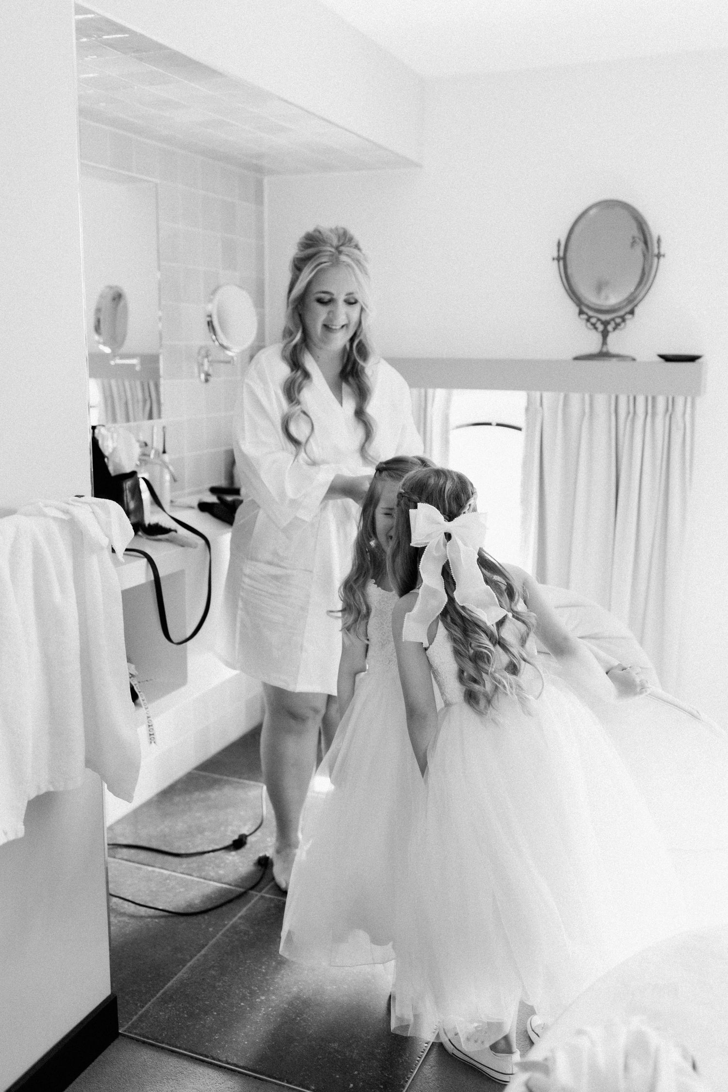 Black and white wedding preparation photos showing someone in a white gown getting ready in a bright interior space.