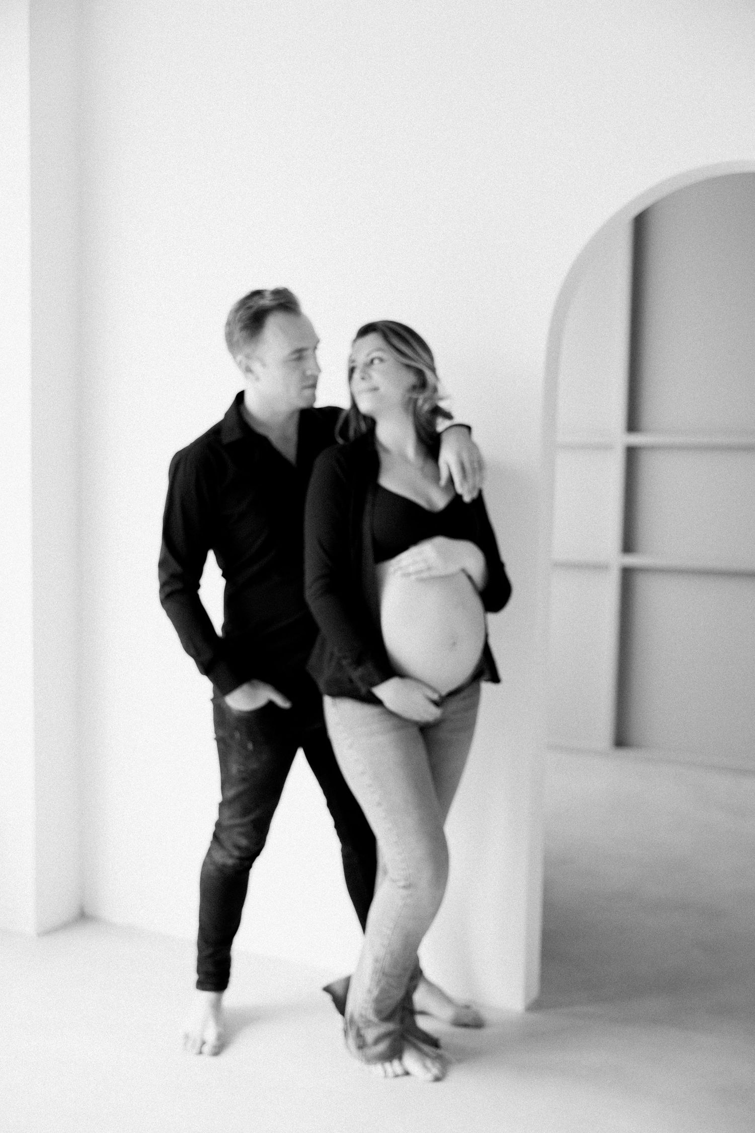 Black and white artistic maternity photo series showing intimate poses against minimalist white backdrop.