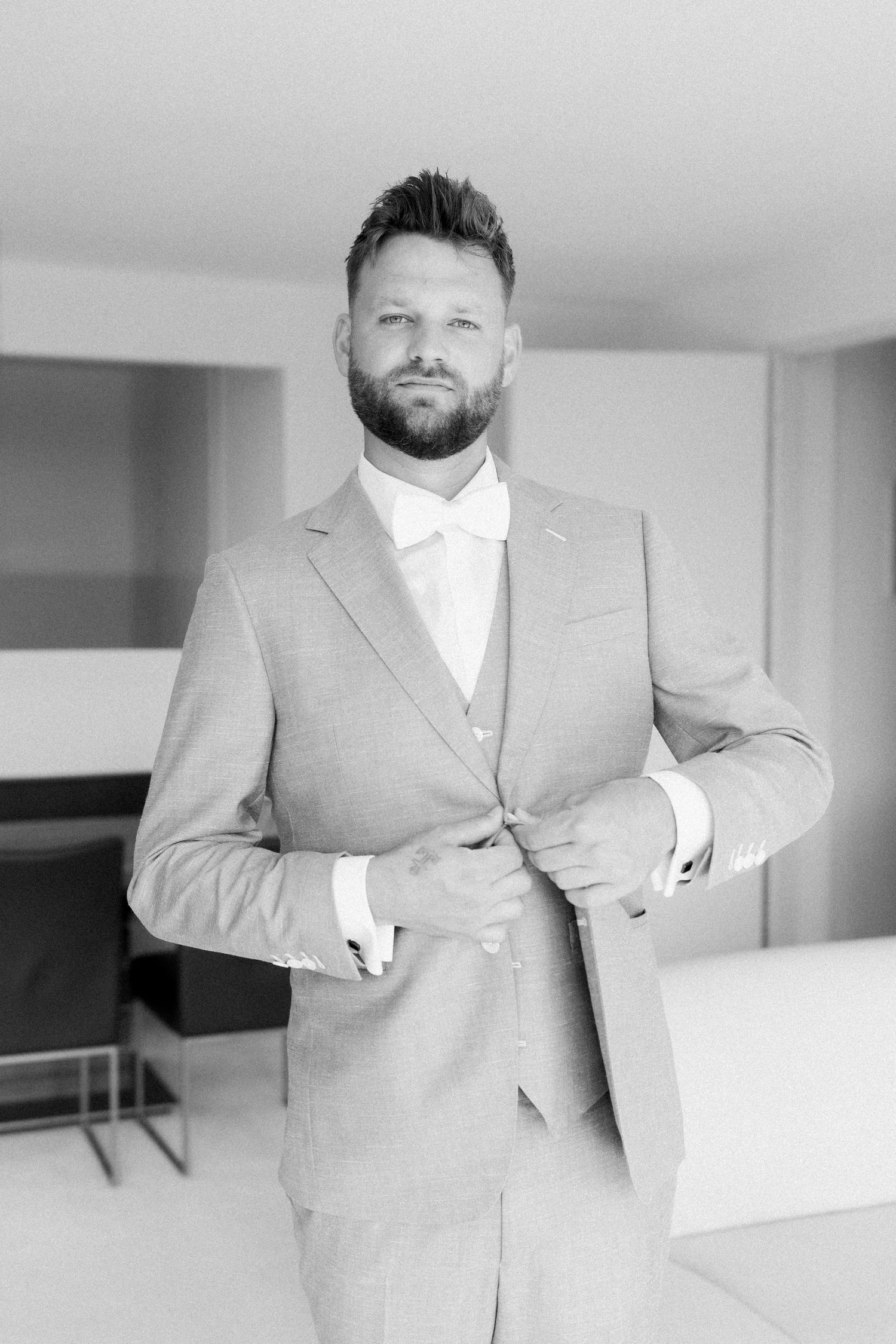 A series of black and white photos showing someone in a light colored suit adjusting their tie and jacket.