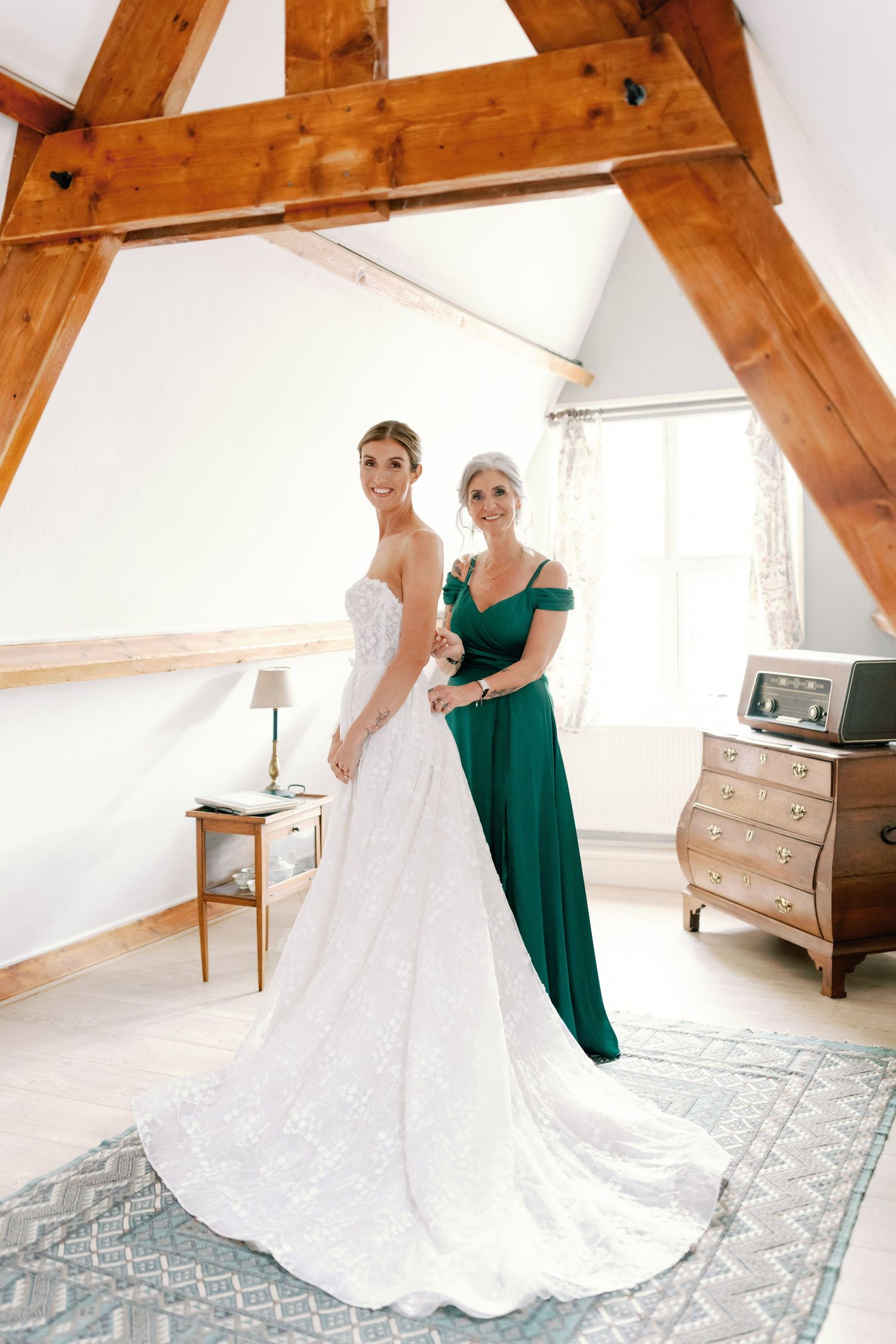 Wedding dress preparation scene in rustic attic room with exposed wooden beams and elegant white gown.