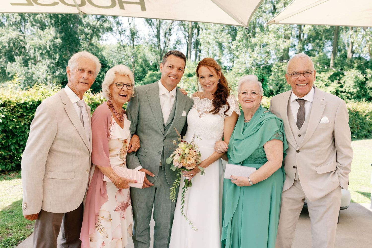 Wedding party poses together outdoors wearing coordinated mint green and beige attire on a sunny day.