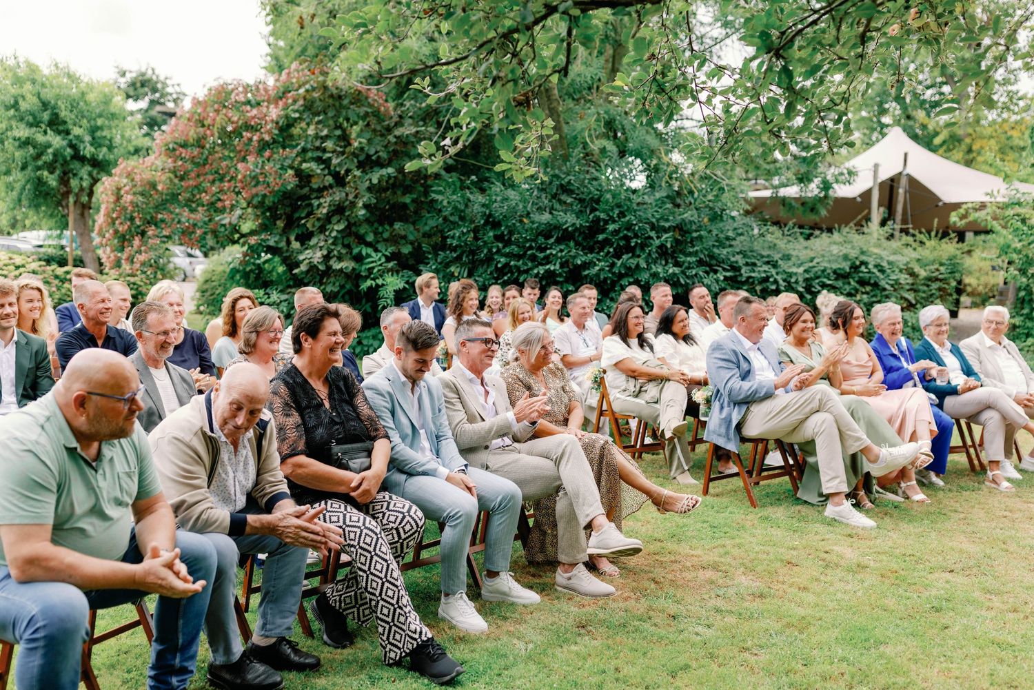 Large group of people sitting in a curved formation on grass during an outdoor gathering.