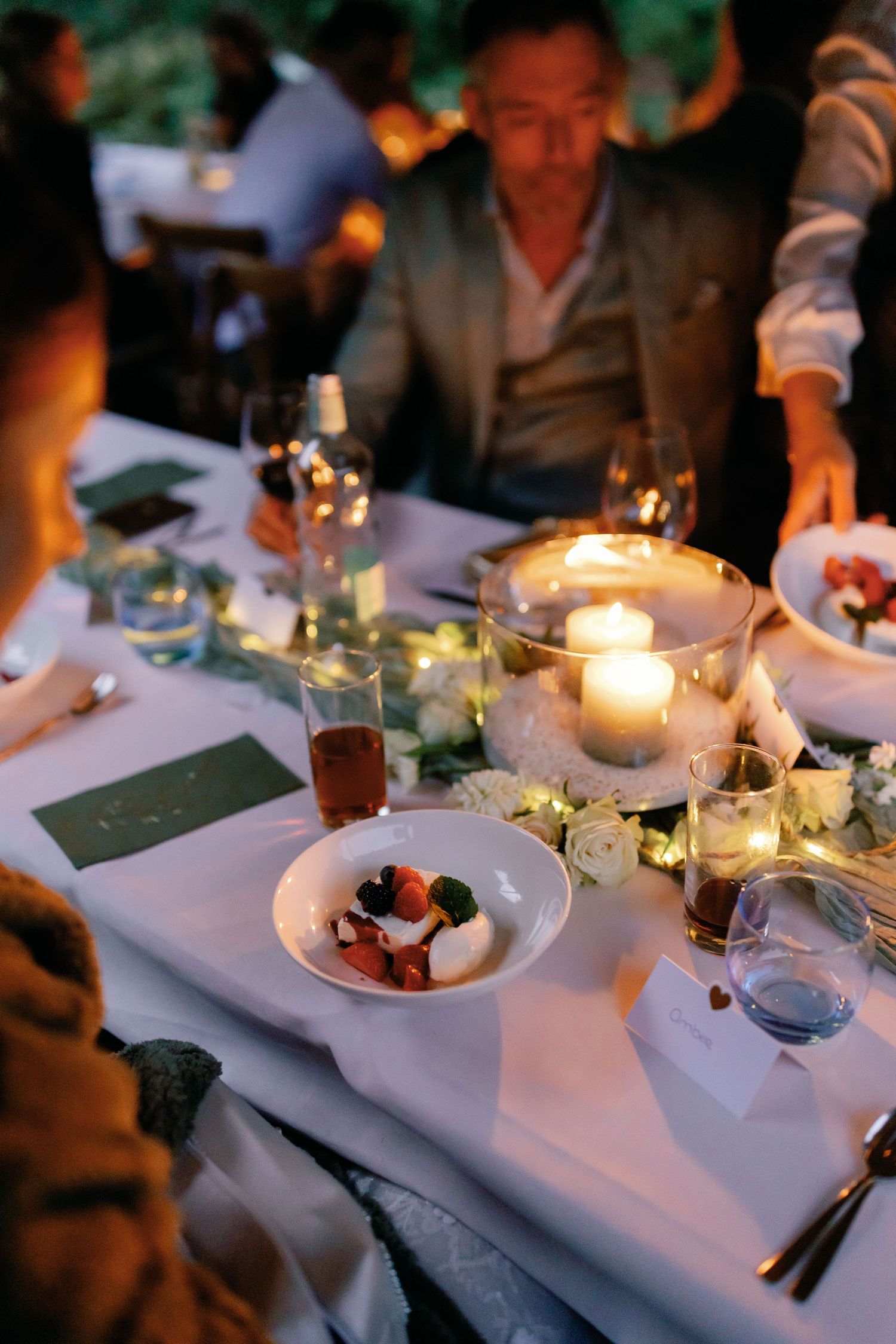 Elegant dinner table settings with glowing candles and white linens at dusk create an intimate dining atmosphere.