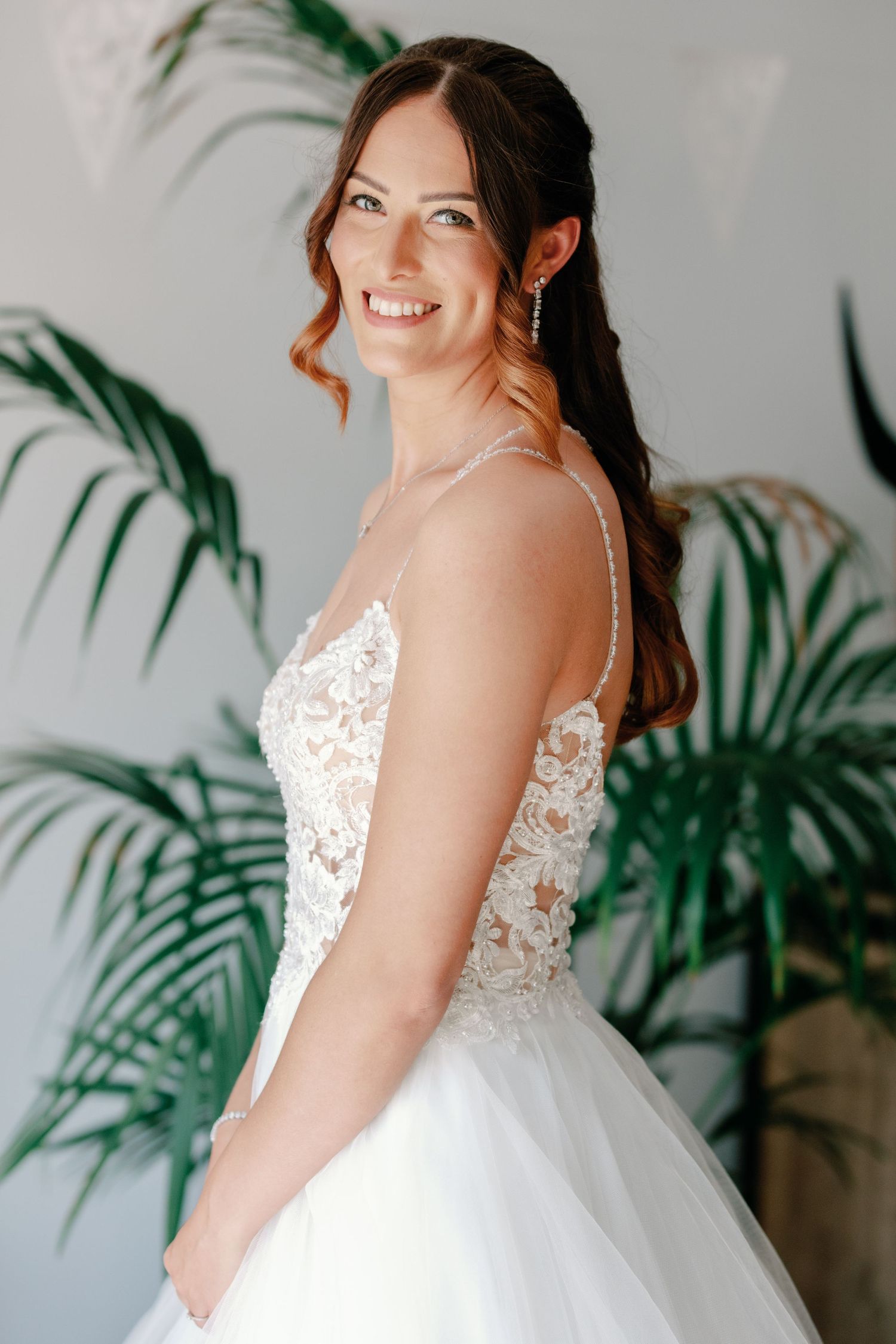 Side profile of someone wearing a white lace bodice wedding gown with tropical plants in background.