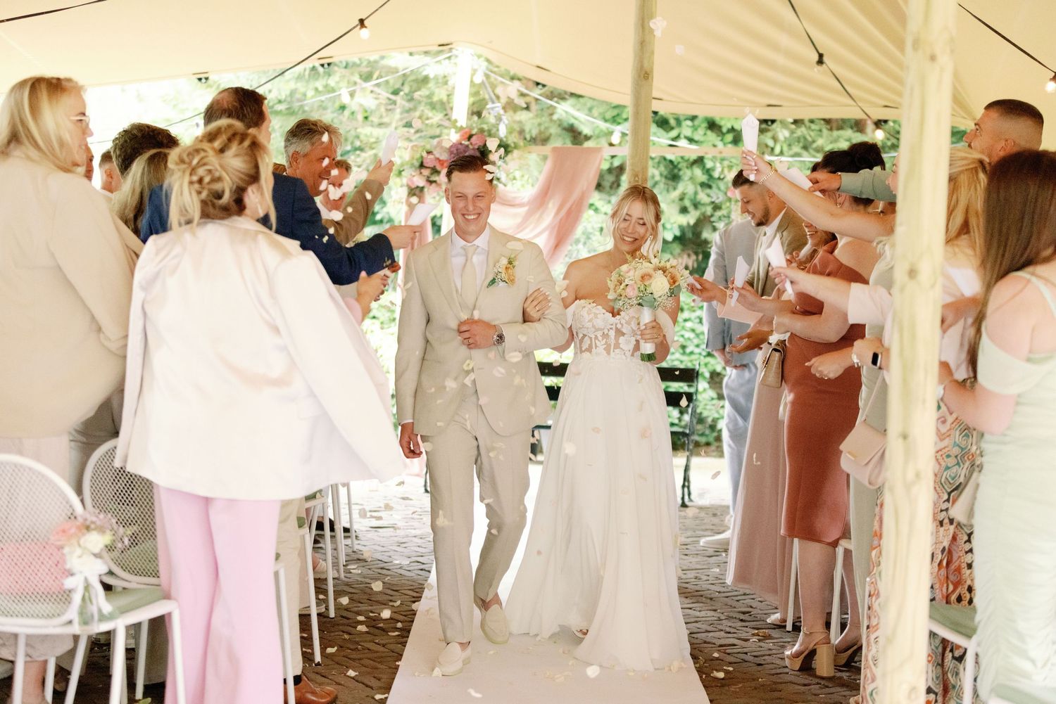 Wedding party dancing and celebrating under a white tent during an outdoor reception celebration.