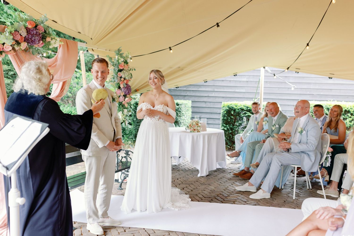 Wedding guests enjoy a reception celebration under an elegant white tent with string lights and decorative accents.