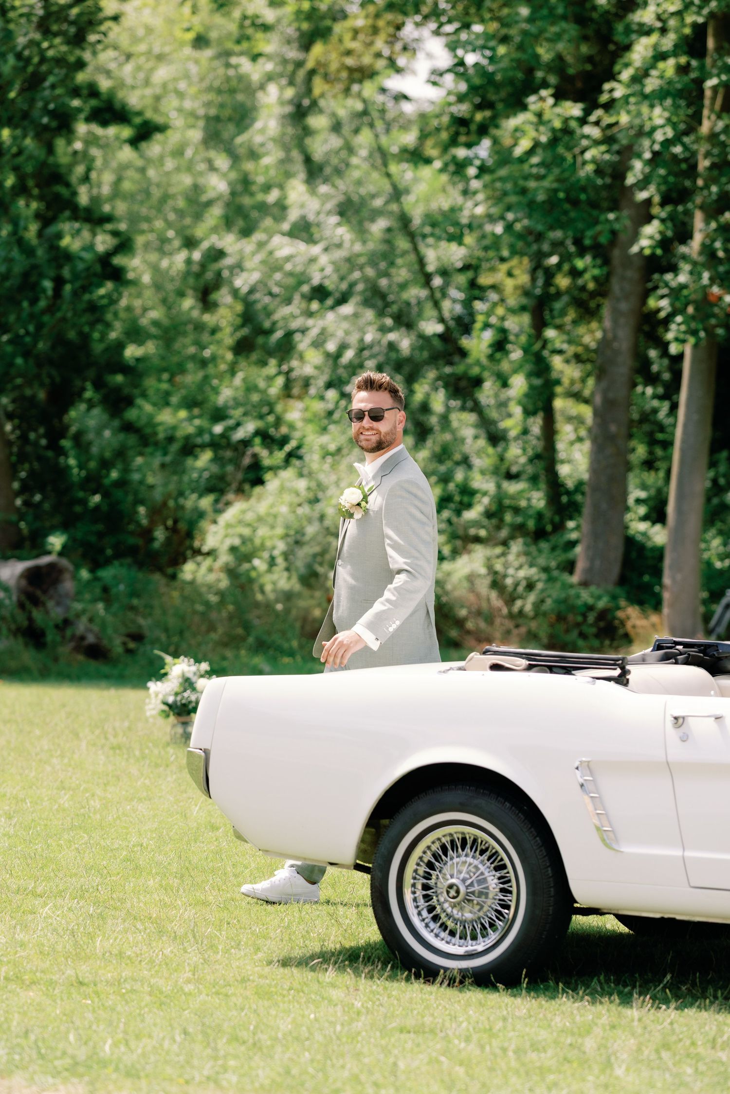 A classic white vintage convertible car parked on a lush green lawn surrounded by trees.