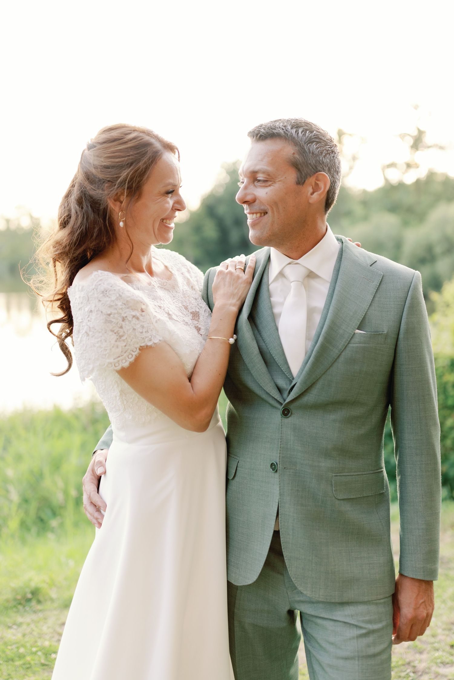 A couple in wedding attire share joyful moments together in a natural outdoor setting during golden hour.