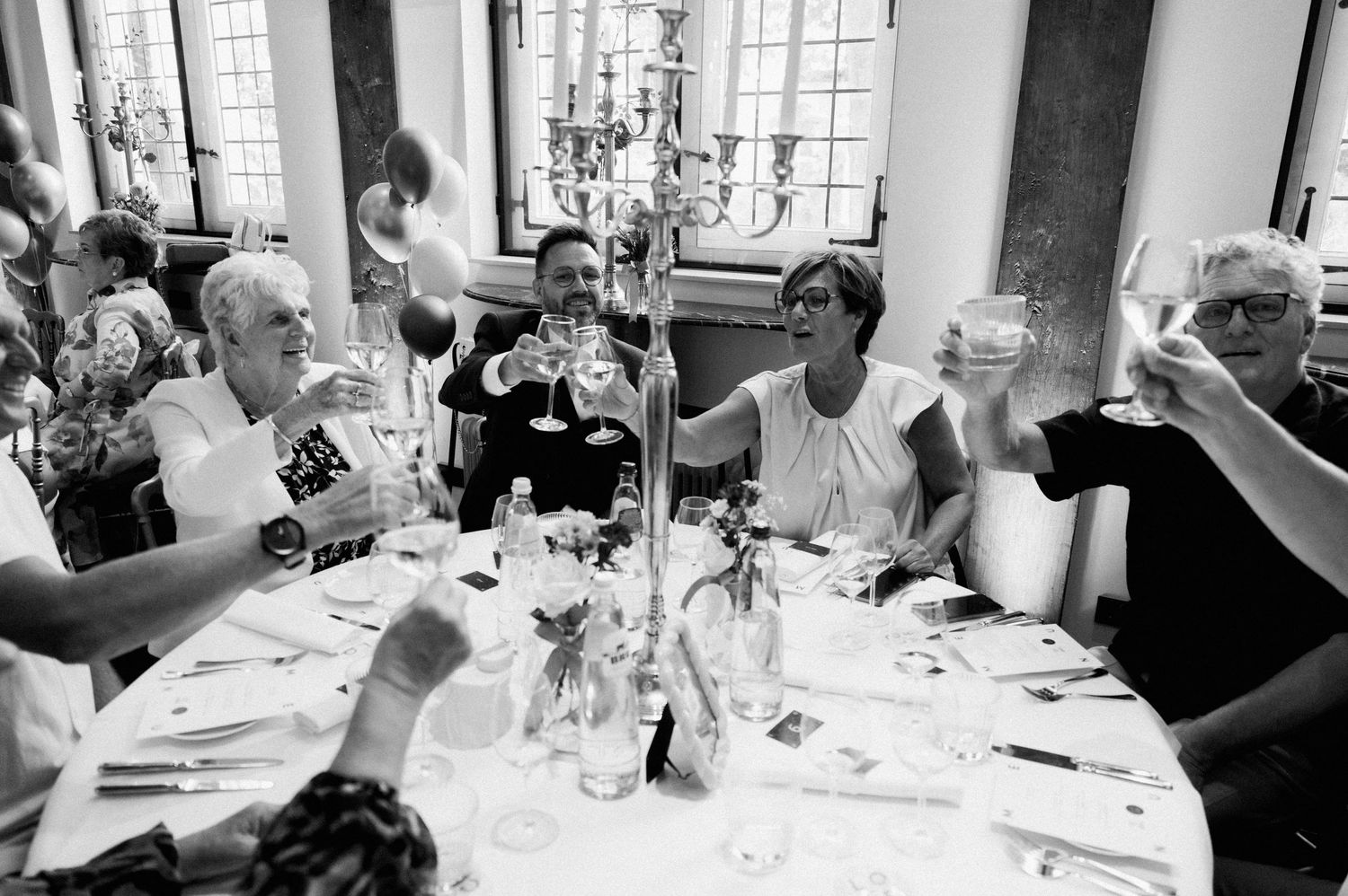 Guests seated at an elegant dinner party table with candles and floral centerpieces engage in lively conversation.