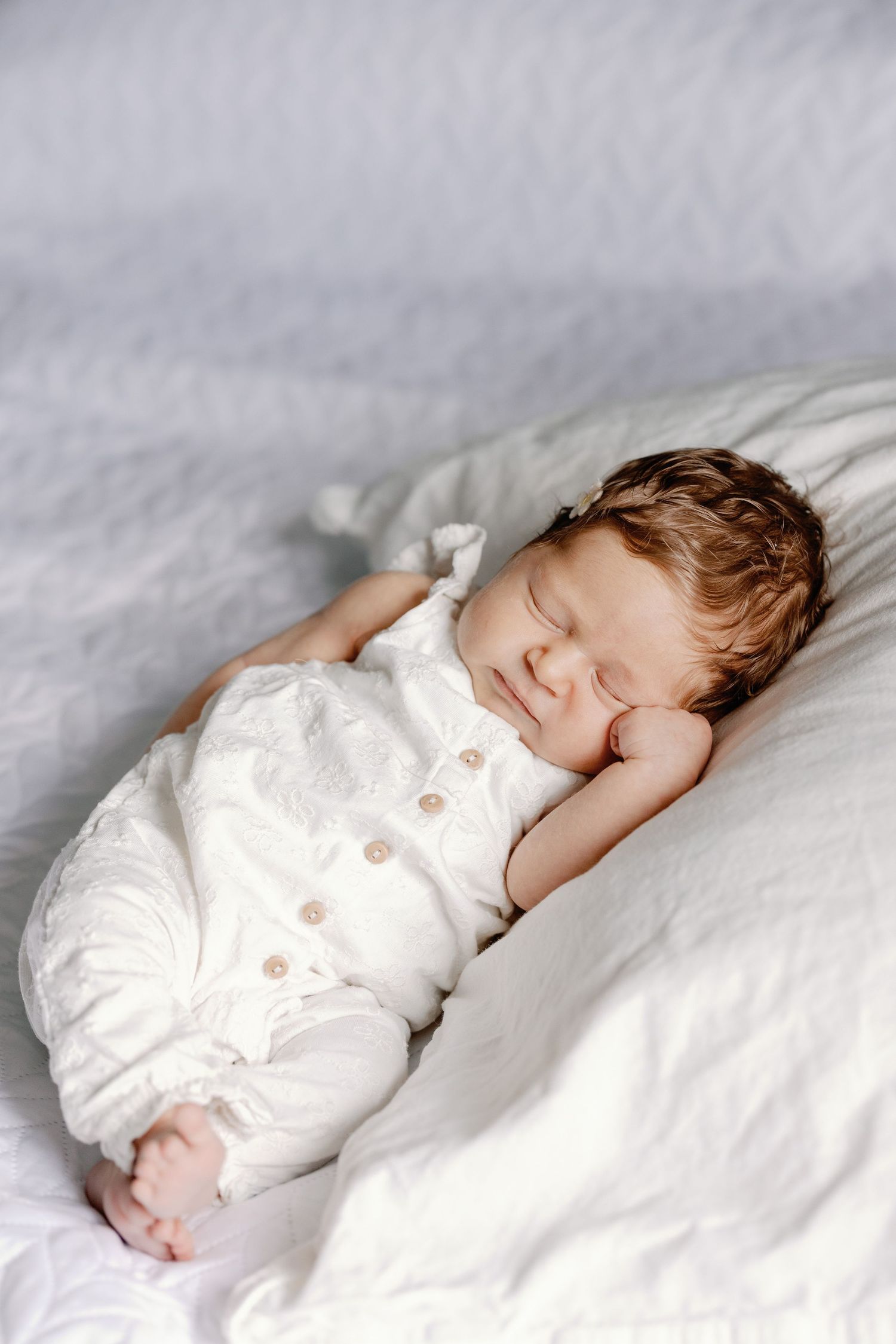A sleeping baby in white clothing rests peacefully on textured white bedding.