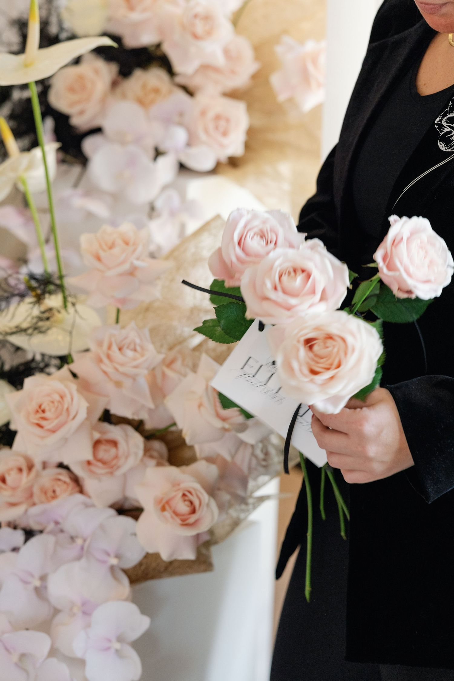 Hands arranging light pink roses in an elegant floral display.