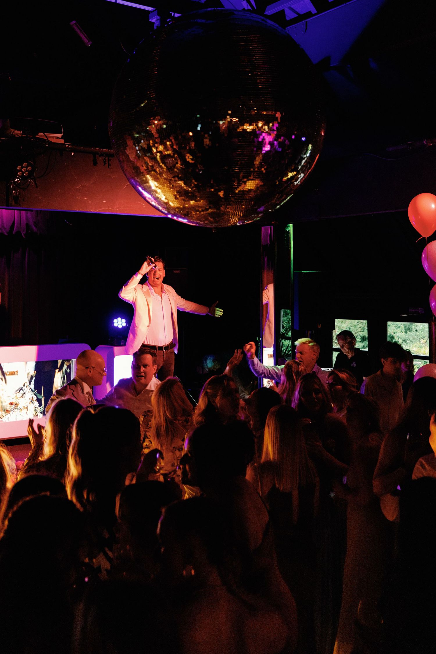 A crowded nightclub scene with silhouettes of people dancing under colorful purple and orange lighting.