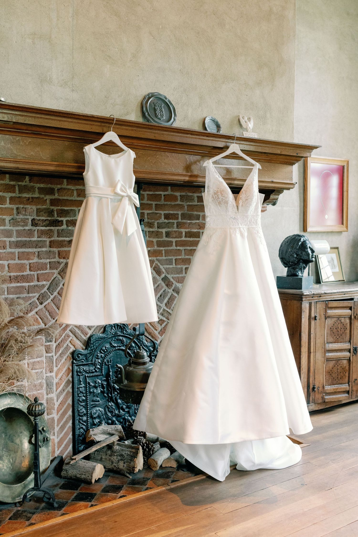 White wedding dresses displayed against a rustic brick wall with antique cast iron stove in a vintage interior setting.