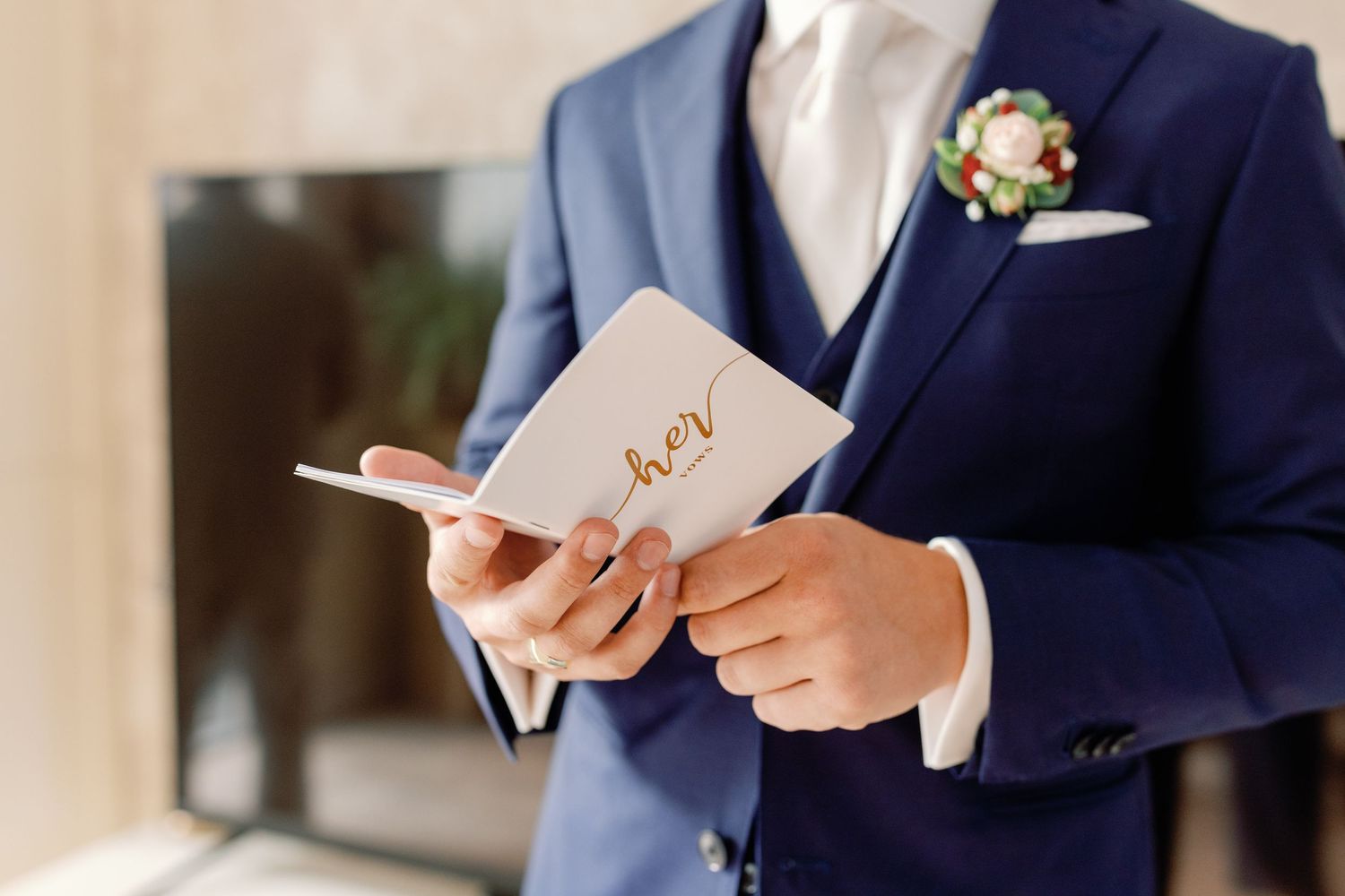 Groom in navy suit reads from a small card during wedding preparations.
