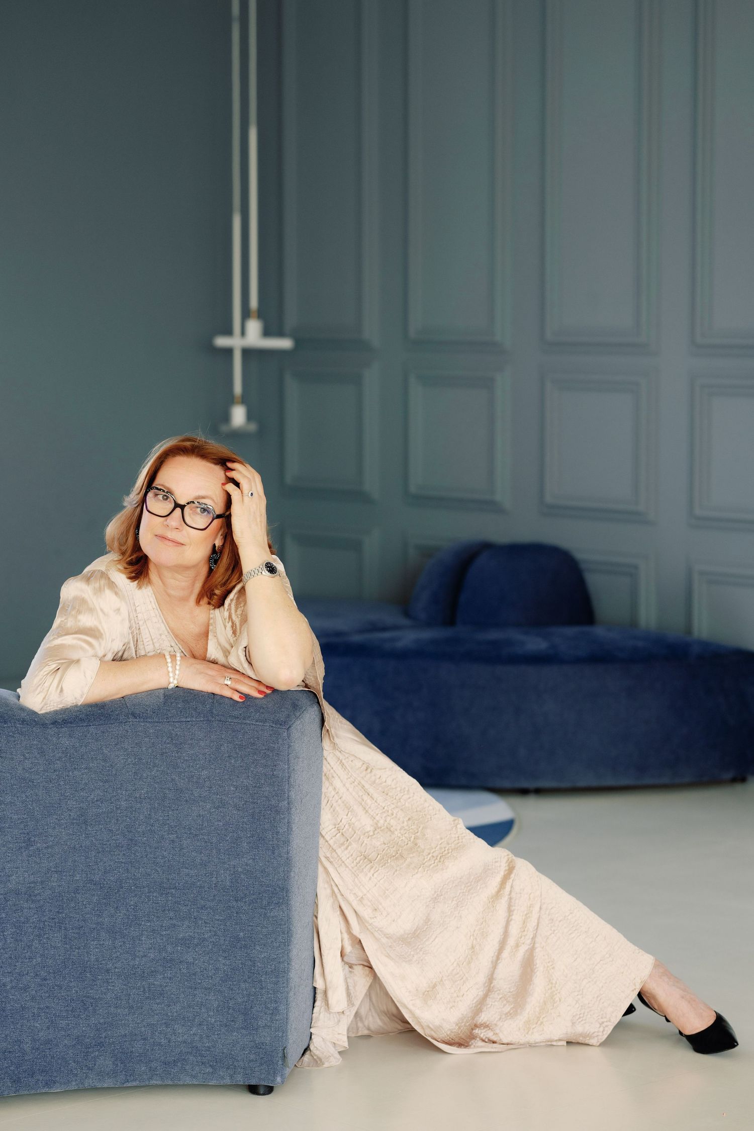 Person in light colored loungewear relaxes on blue couch in minimalist room with white walls.