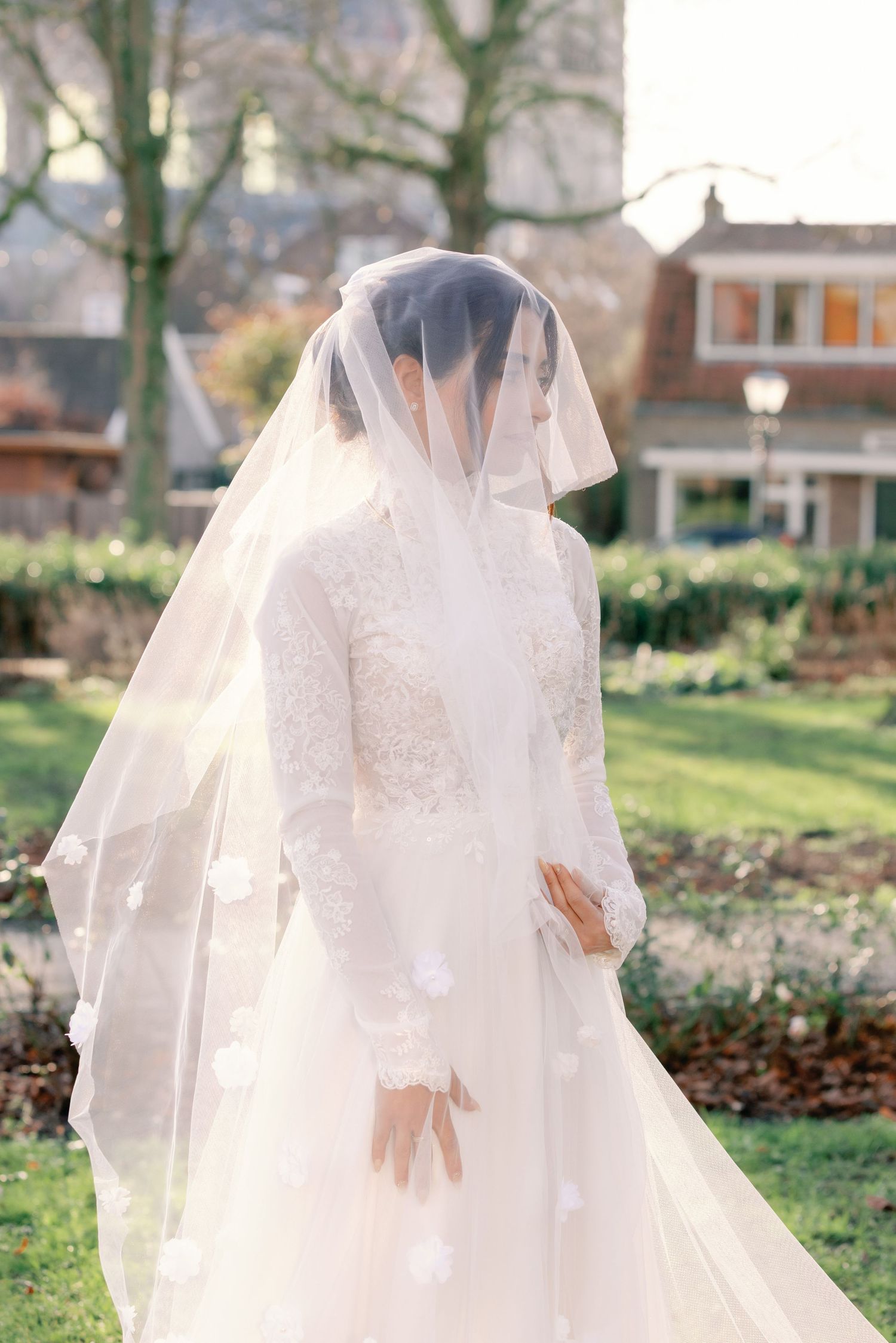 A flowing white wedding veil catches the breeze in a garden setting during a bridal photoshoot.