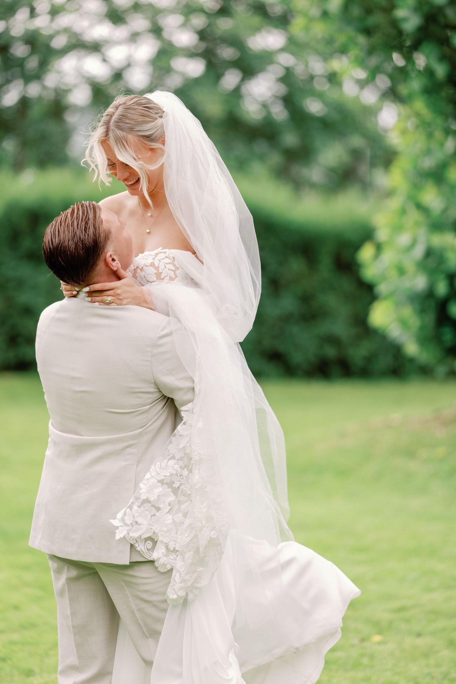A tender wedding moment captured in a garden setting with flowing white dress and veil.