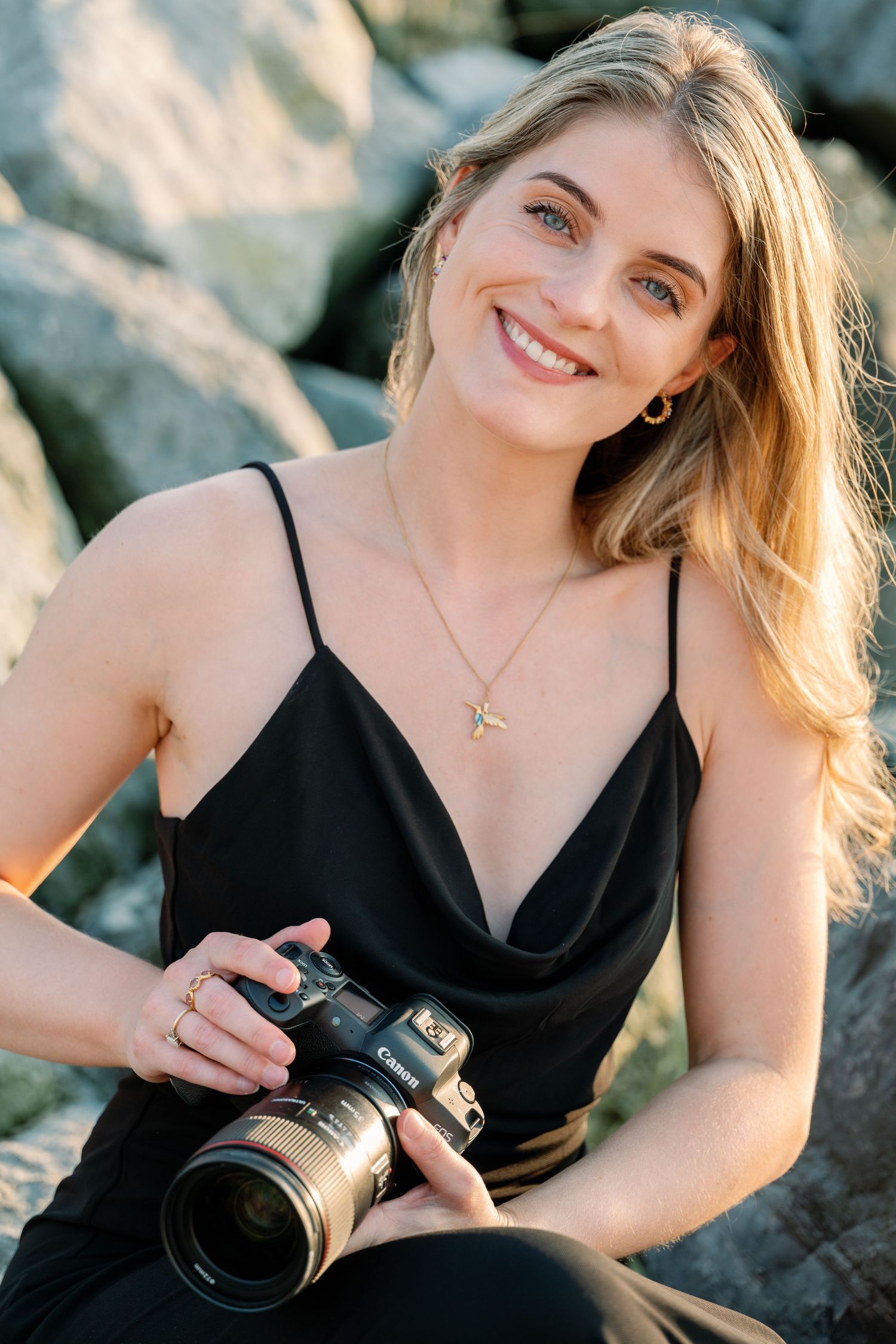Professional photographer in black dress holding camera outdoors.