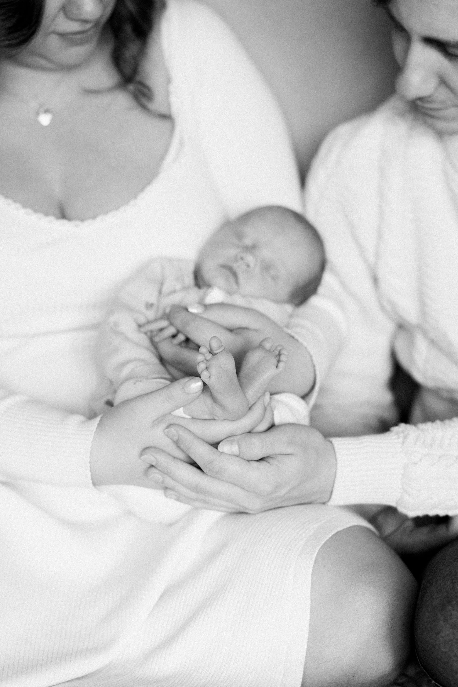 Close-up black and white images showing tender moments with a newborn baby in white blankets.