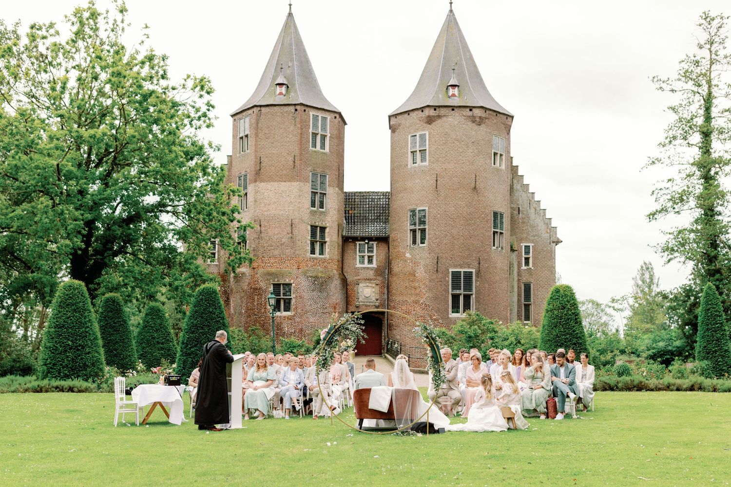 Beautiful castle-like venue with twin spires hosts an outdoor wedding celebration on sprawling green lawn.