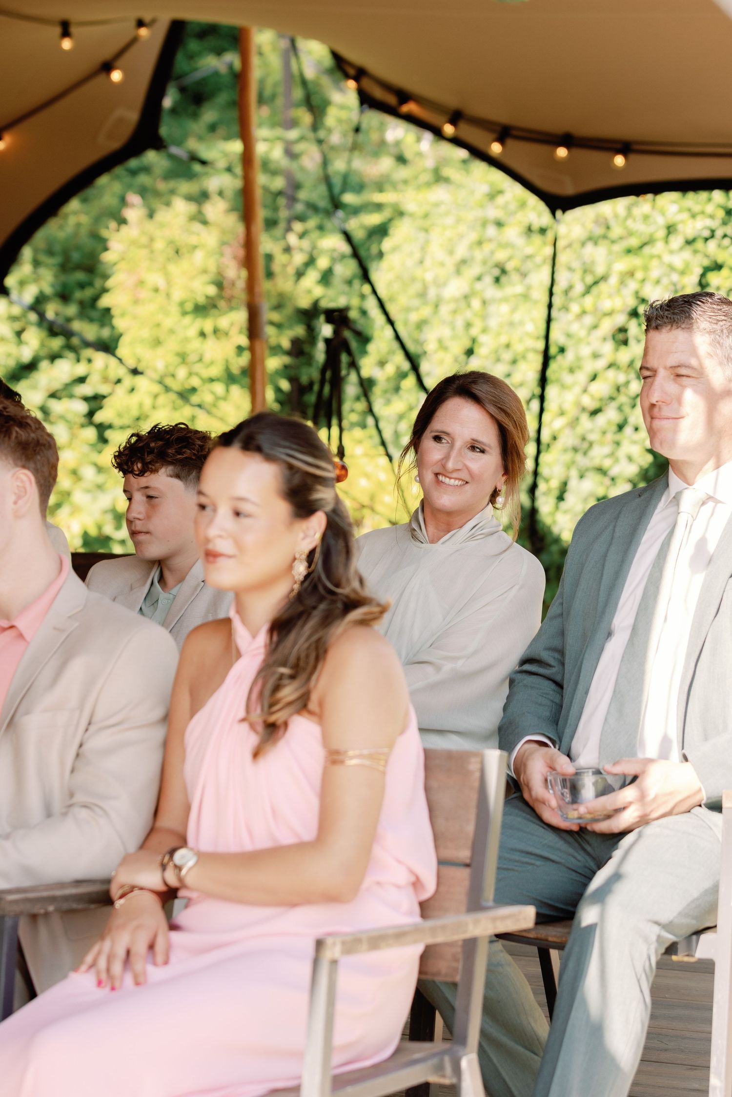 Wedding guests seated under a canopy with string lights during an outdoor ceremony.